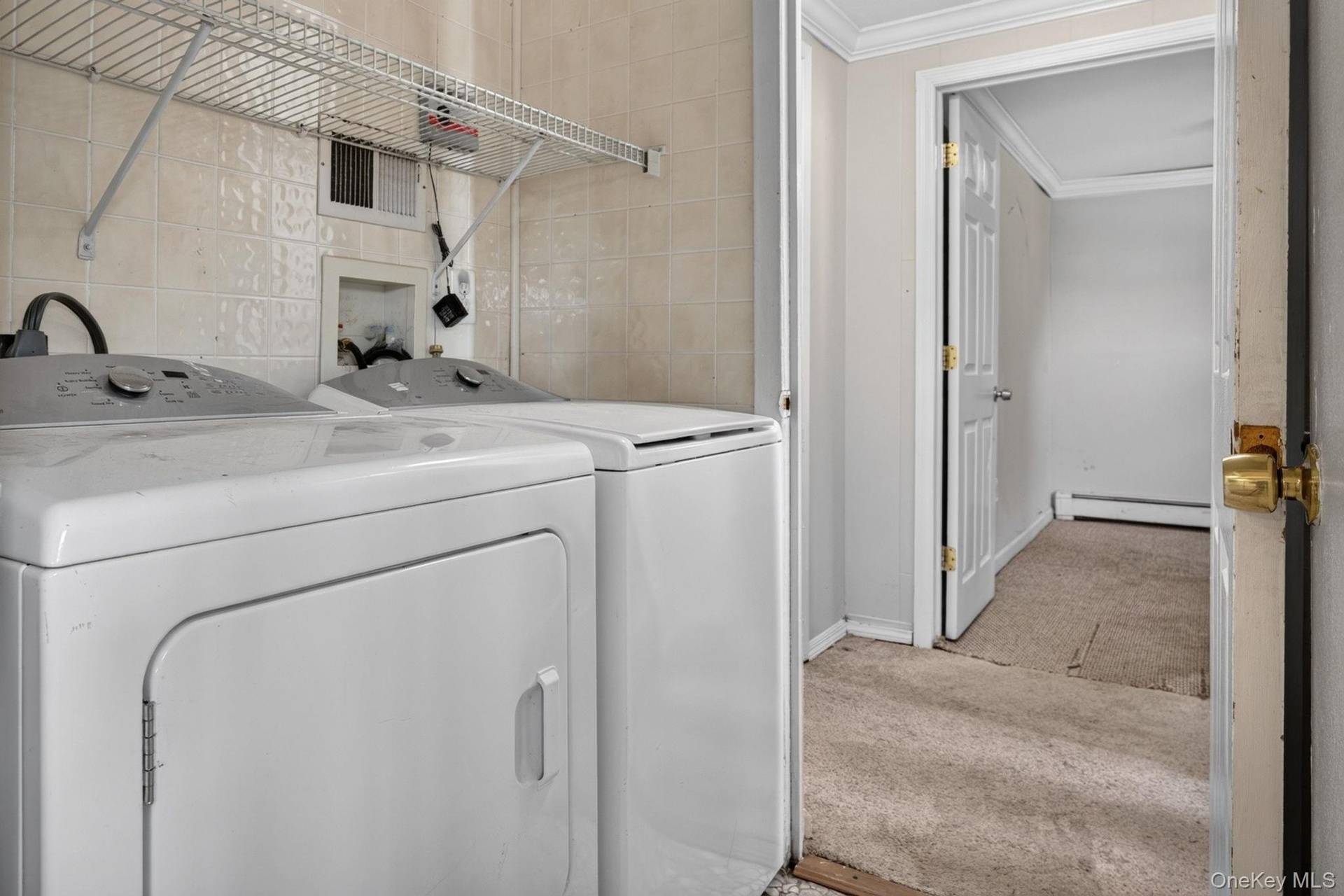 Dedicated laundry area featuring a washer and dryer set, tiled wall, and wire shelving