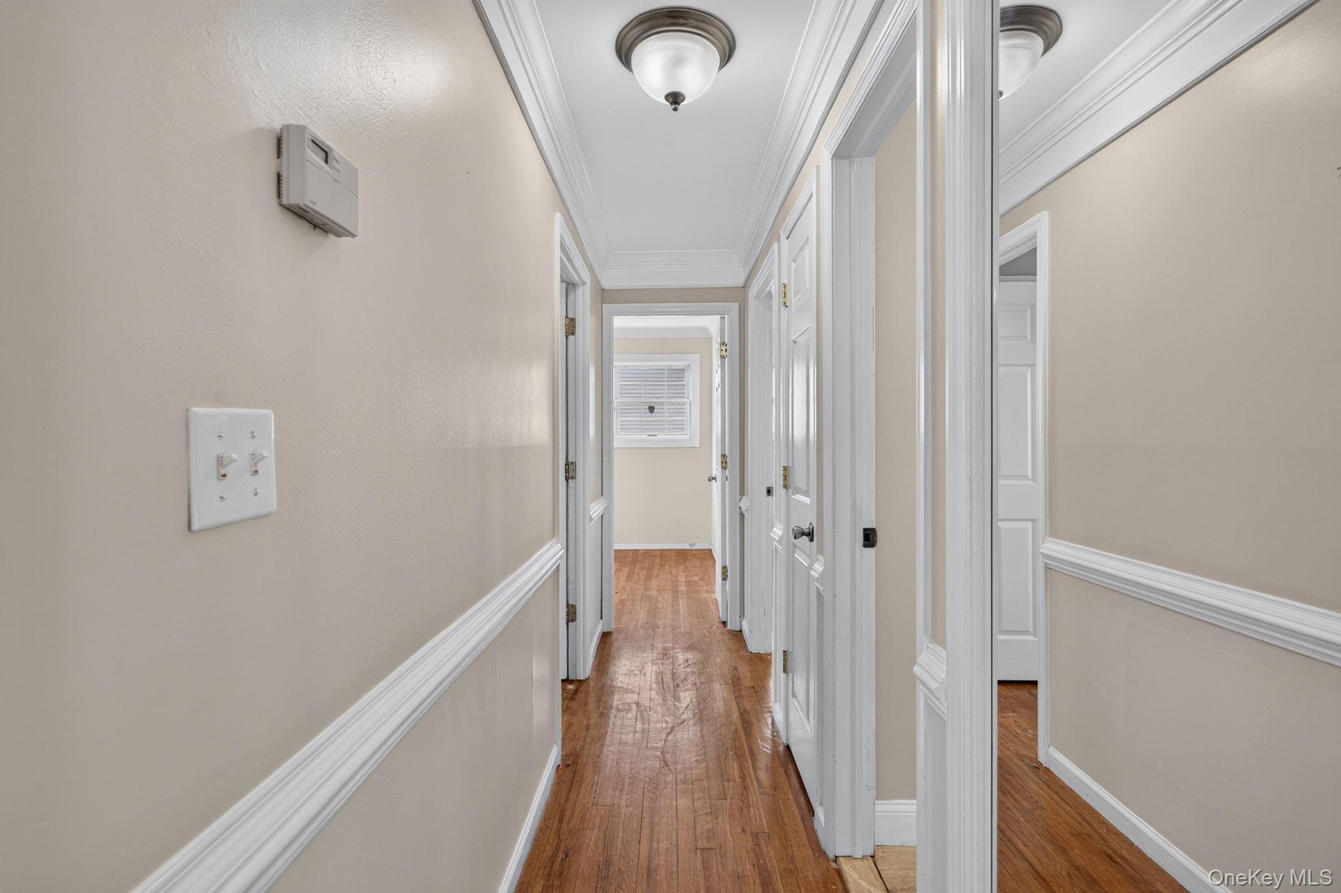 Hallway featuring wood-finish flooring, light-toned walls with chair rail molding, and white trim