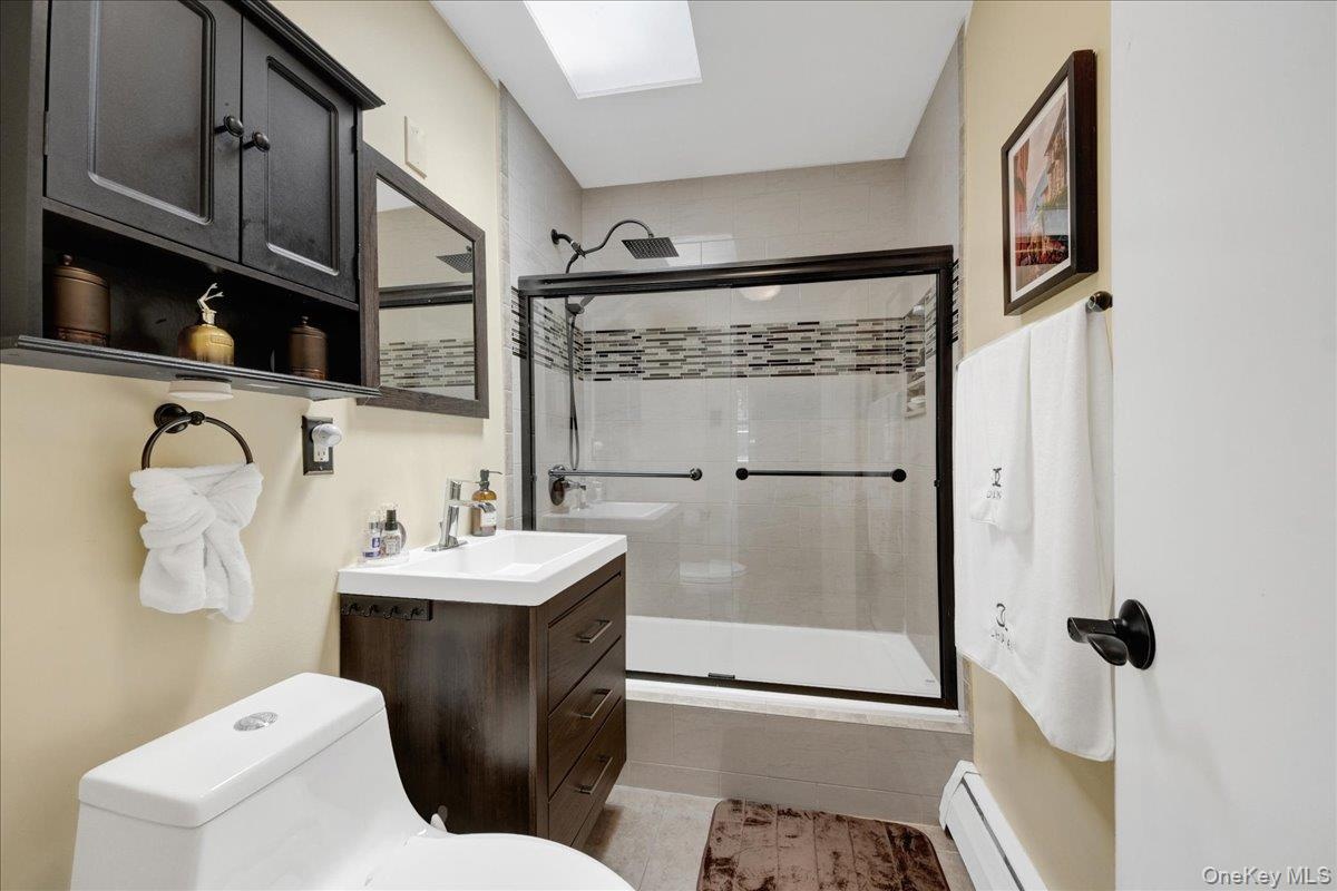 Full bathroom featuring a skylight & dark wood-finish vanity with an integrated white sink.