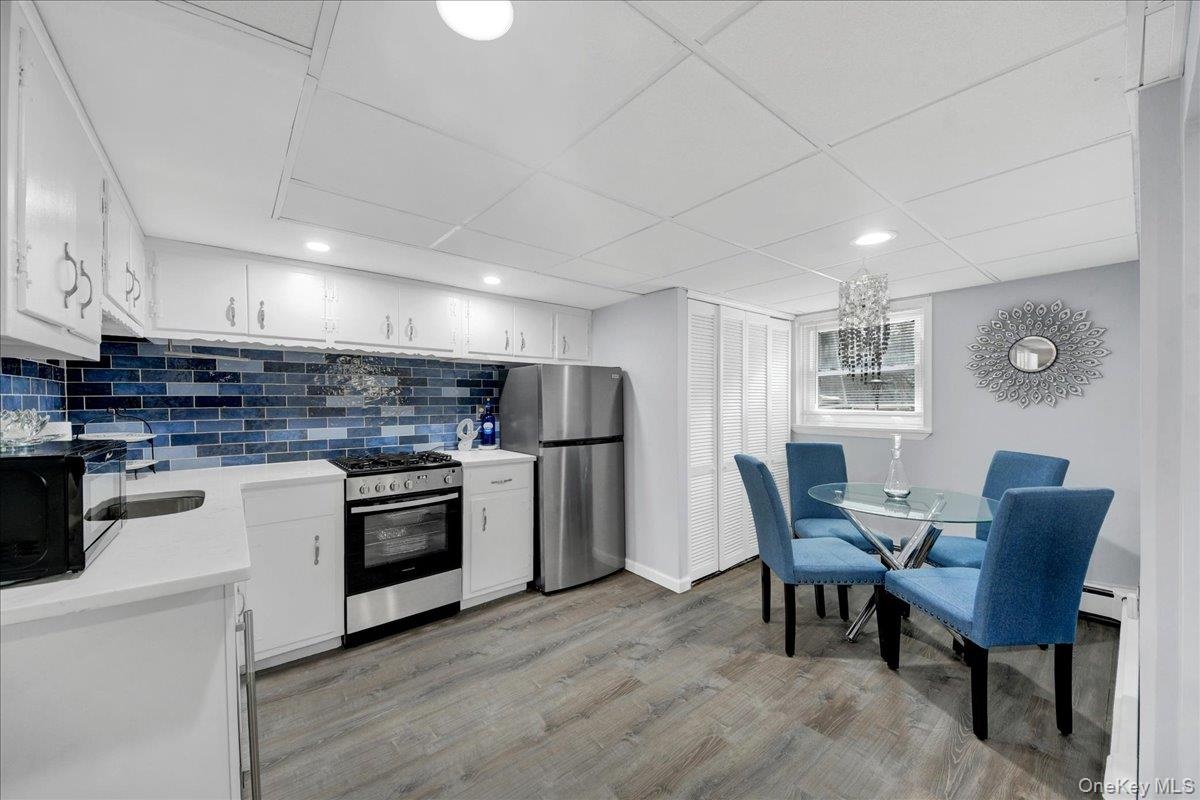 Kitchen and dining area featuring white cabinetry, a blue subway tile backsplash, stainless steel appliances