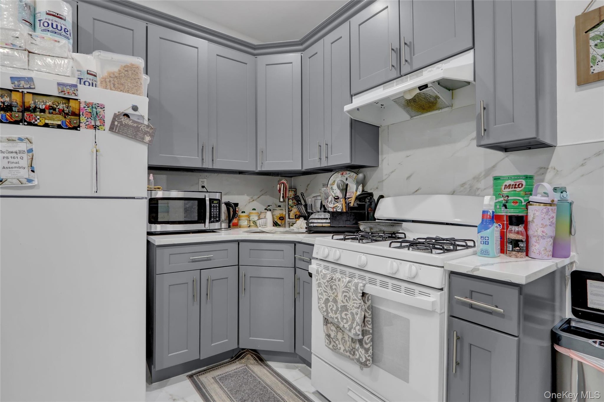 Kitchen featuring gray shaker-style cabinetry, white countertops, and a white marble-look tile backsplash