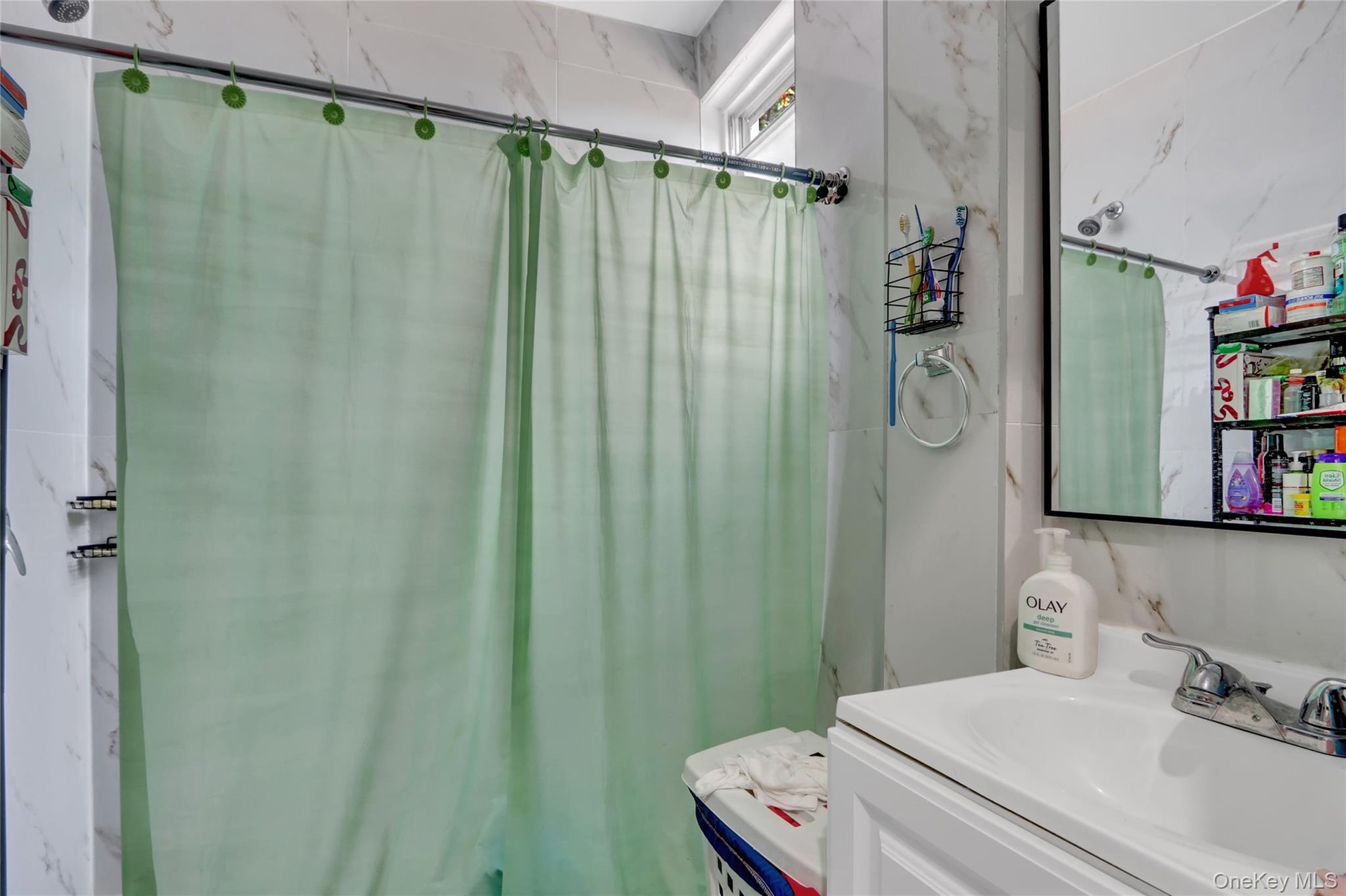 Bathroom featuring white marble-look wall tiles, a white vanity with a ceramic sink, a rectangular framed mirror, and a window providing natural light