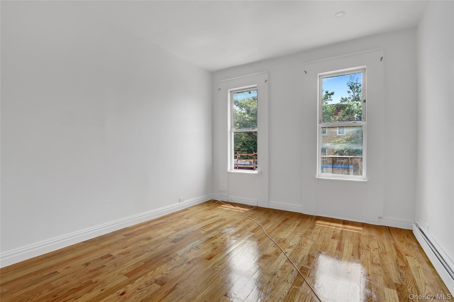 Room featuring two large windows, wood-finish flooring, white baseboards, and white painted walls