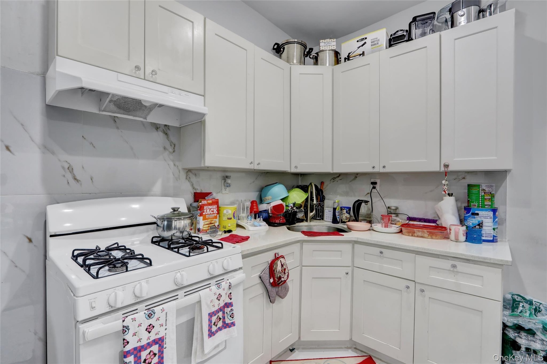 Kitchen featuring white flat-panel cabinetry, white countertops, a white gas range with four burners, a white range hood, and a white and gray veined 