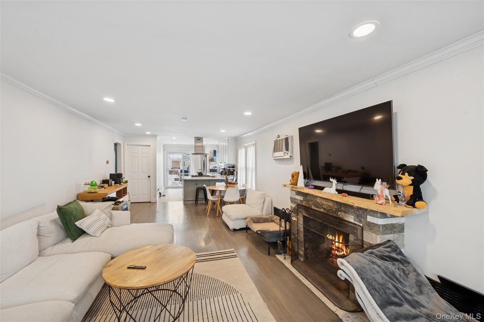 Living area featuring crown molding, a stone fireplace, wood finished floors, and recessed lighting
