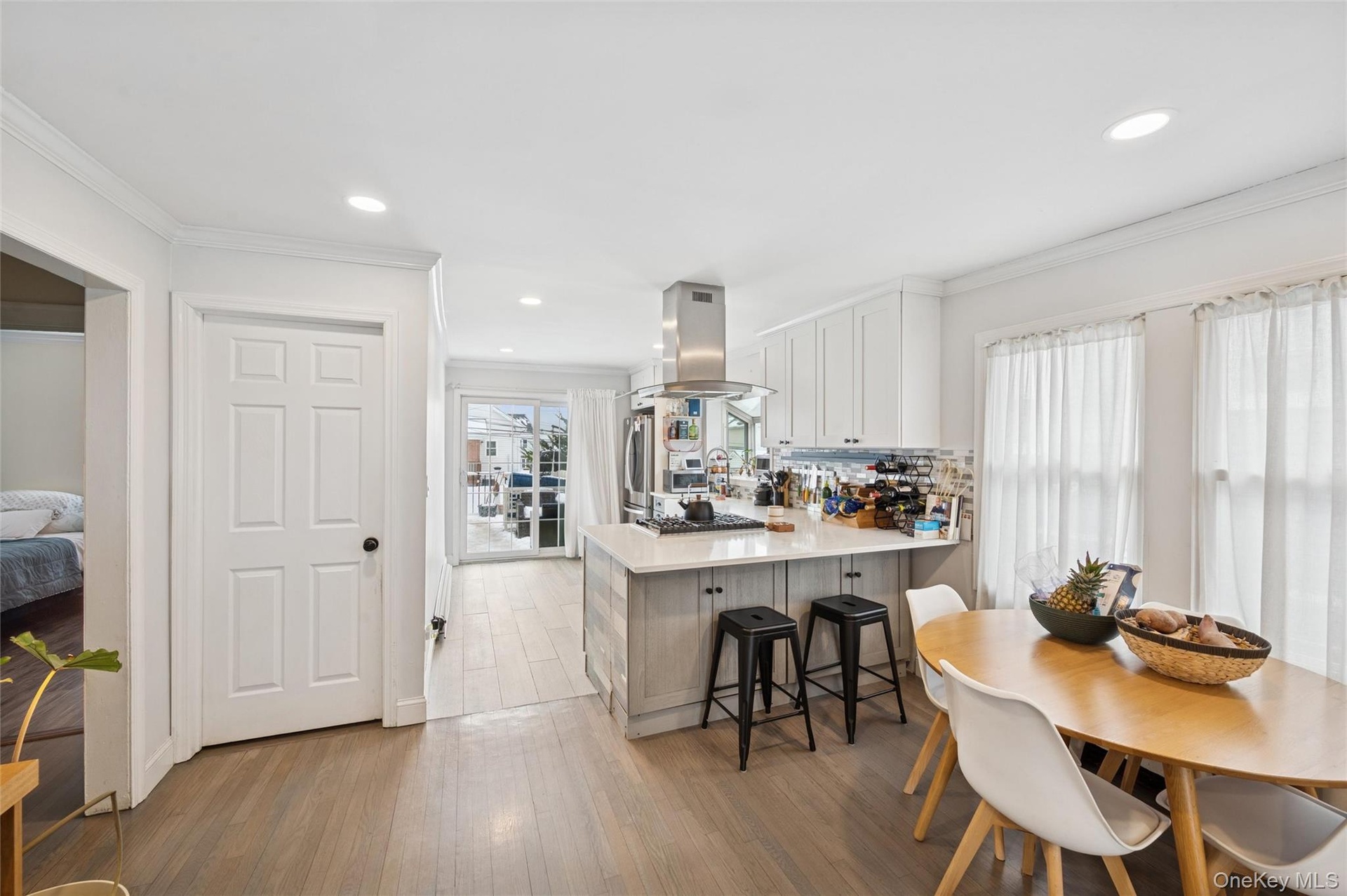 Kitchen featuring crown molding, light wood finished floors, a peninsula, white cabinets, and island range hood