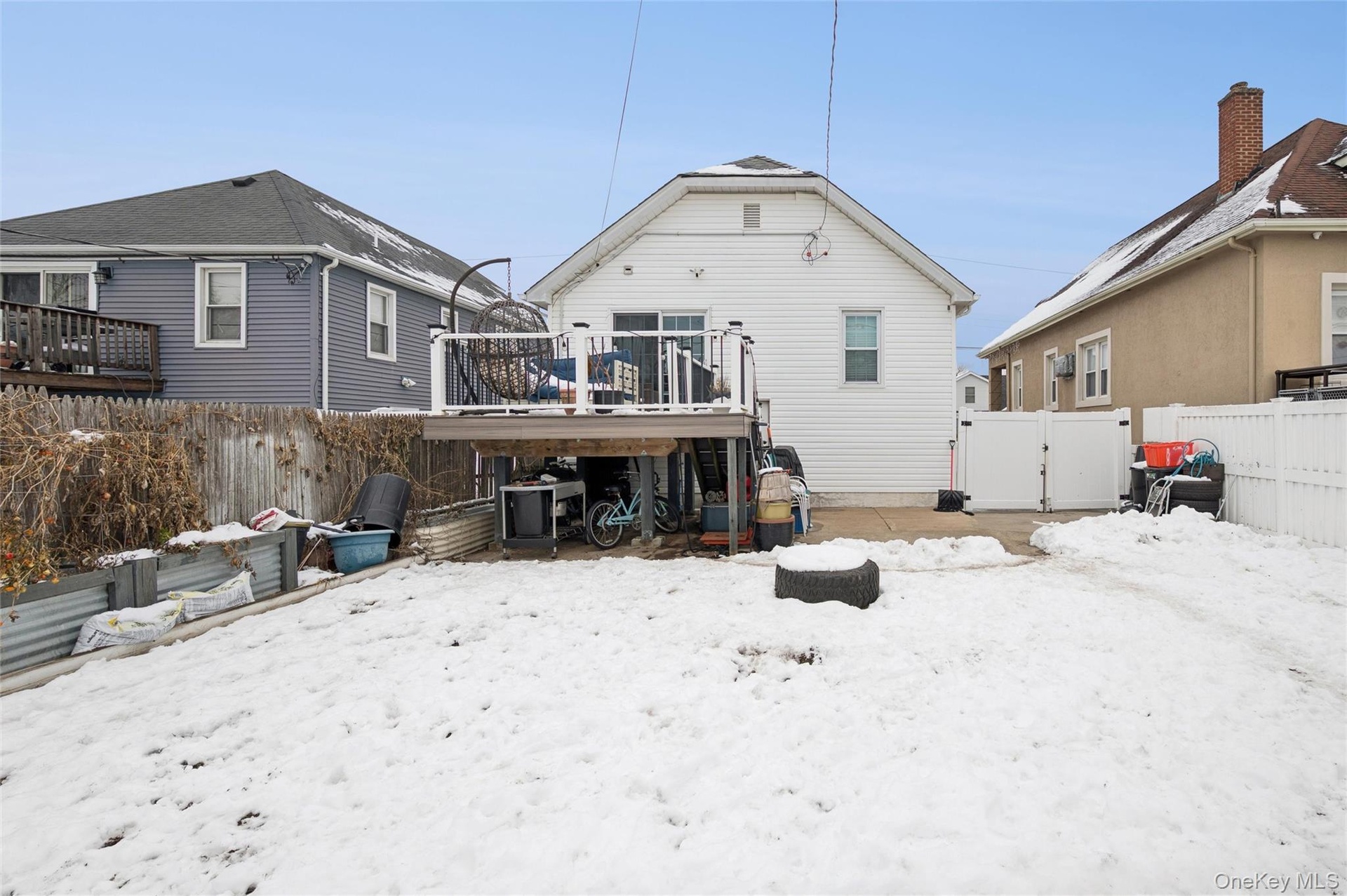 Snow covered house with a fenced backyard, a gate, a deck, and a patio