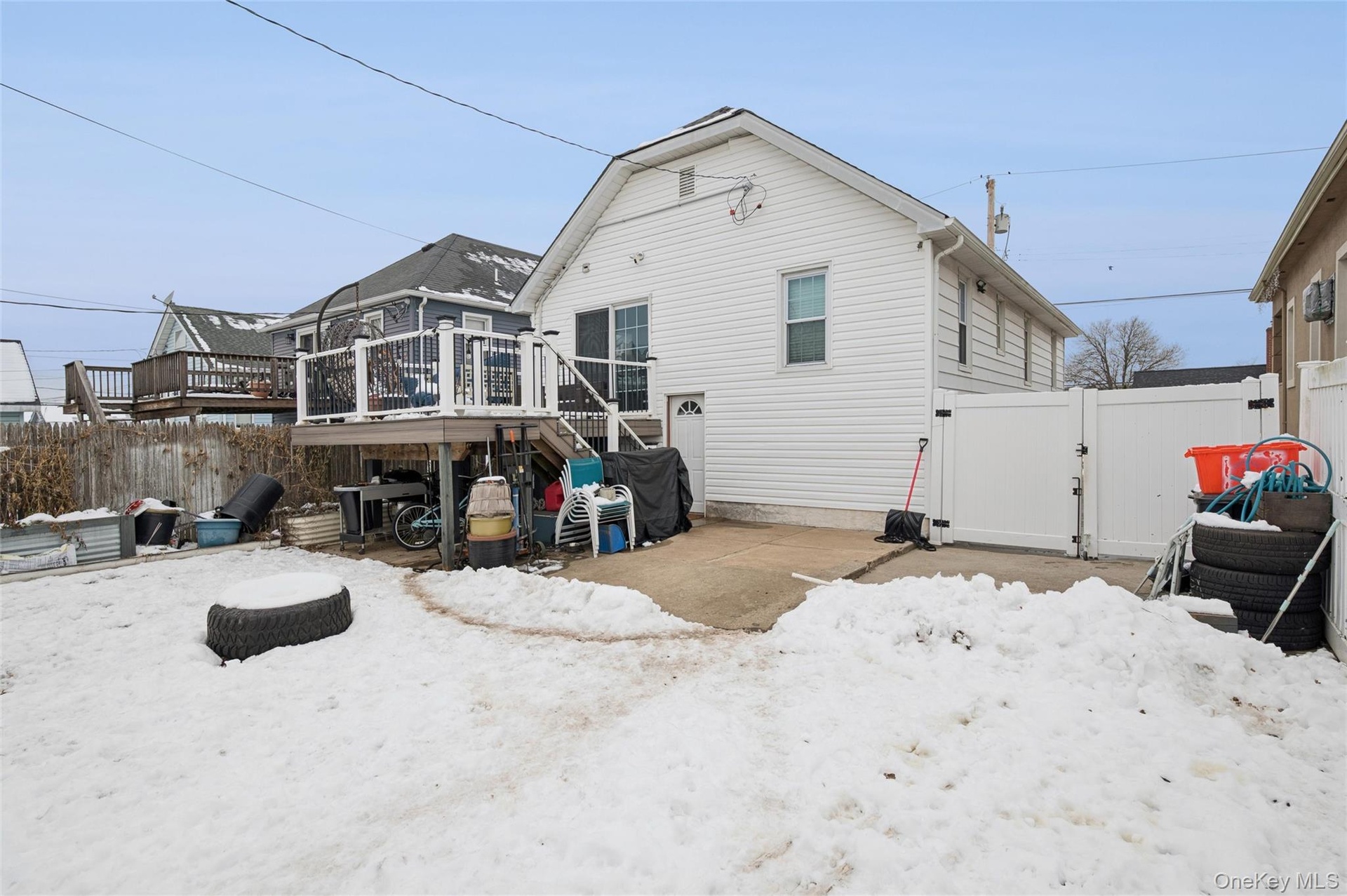 Snow covered rear of property featuring a gate, a wooden deck, a patio area, and stairs