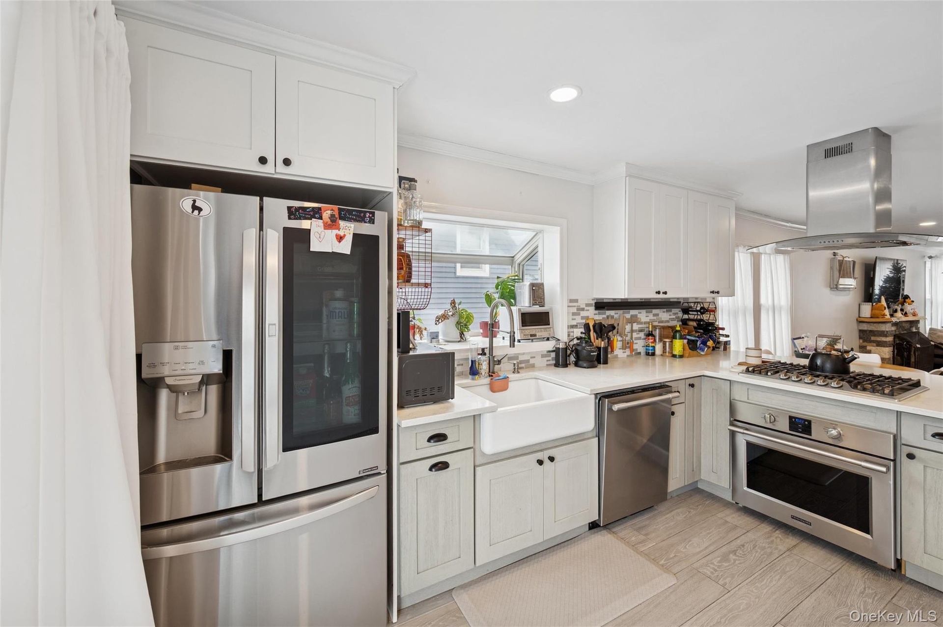 Kitchen with appliances with stainless steel finishes, ornamental molding, island exhaust hood, light wood-style floors, and white cabinets