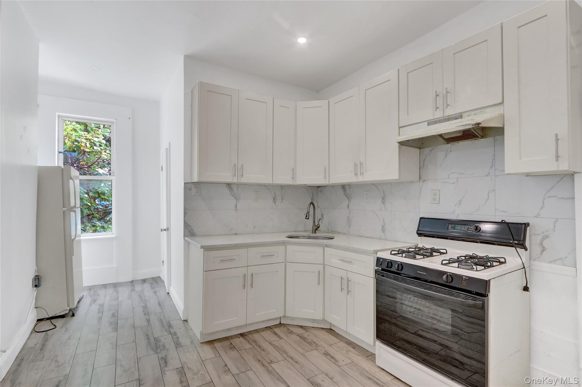 Kitchen featuring white cabinetry, light-toned countertops, a white subway tile backsplash, and wood-finish flooring