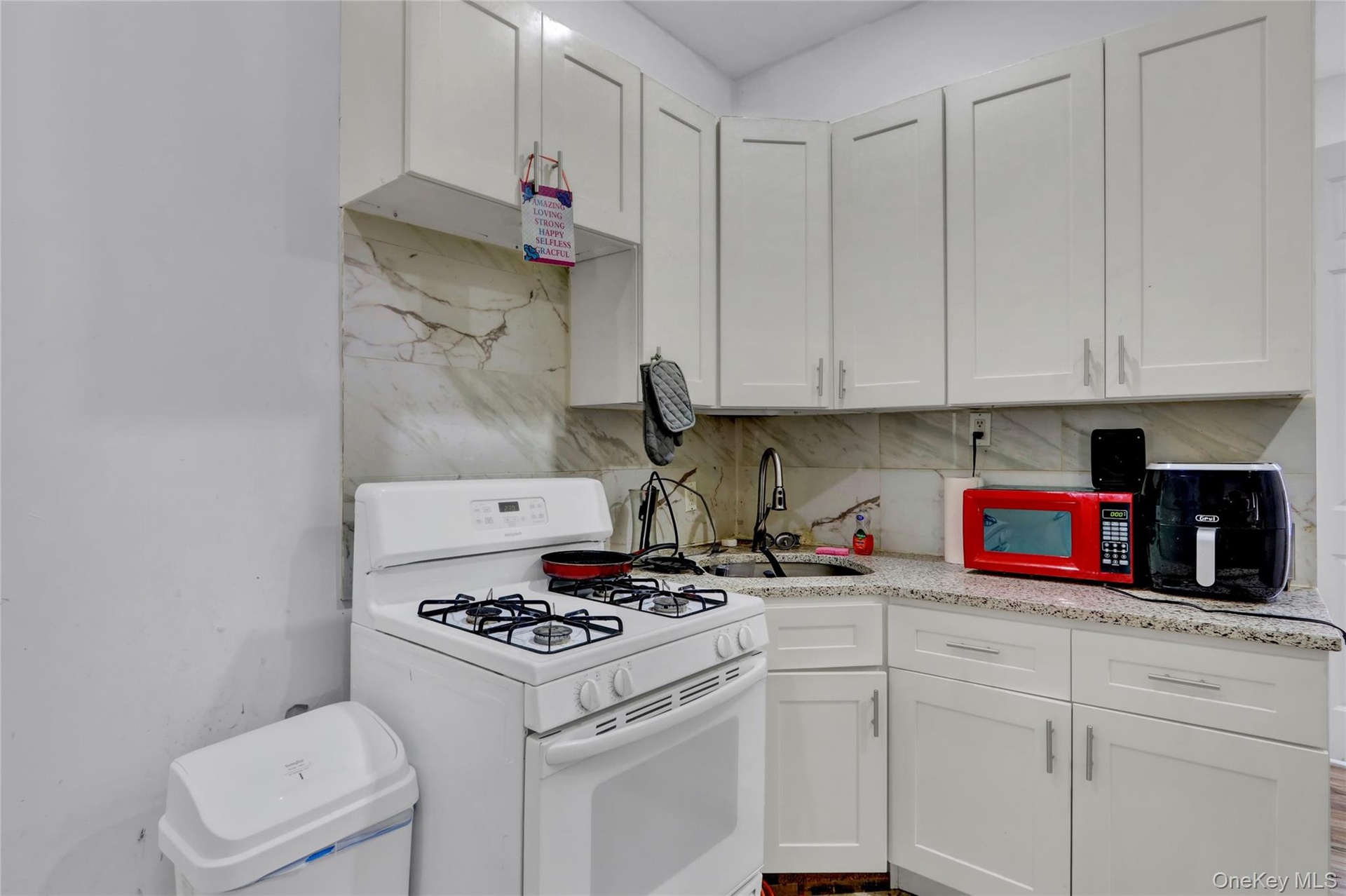 Kitchen featuring white cabinetry, a gas range, a stainless steel sink with a gooseneck faucet, light-toned countertops, and a patterned backsplash
