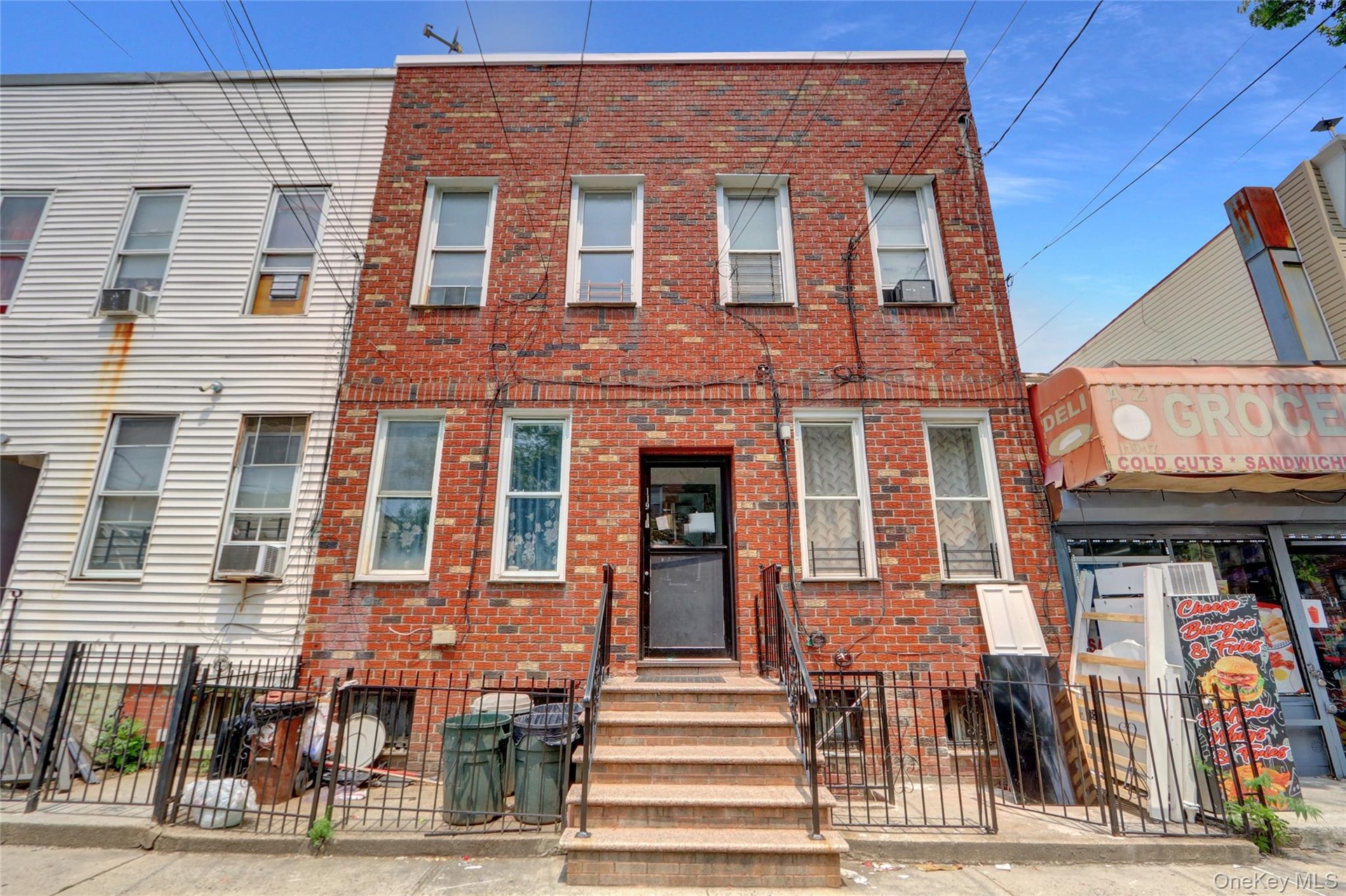 Three-story brick facade property featuring multiple windows with security bars, a ground-level entryway with a dark door, and exterior stairs with bl