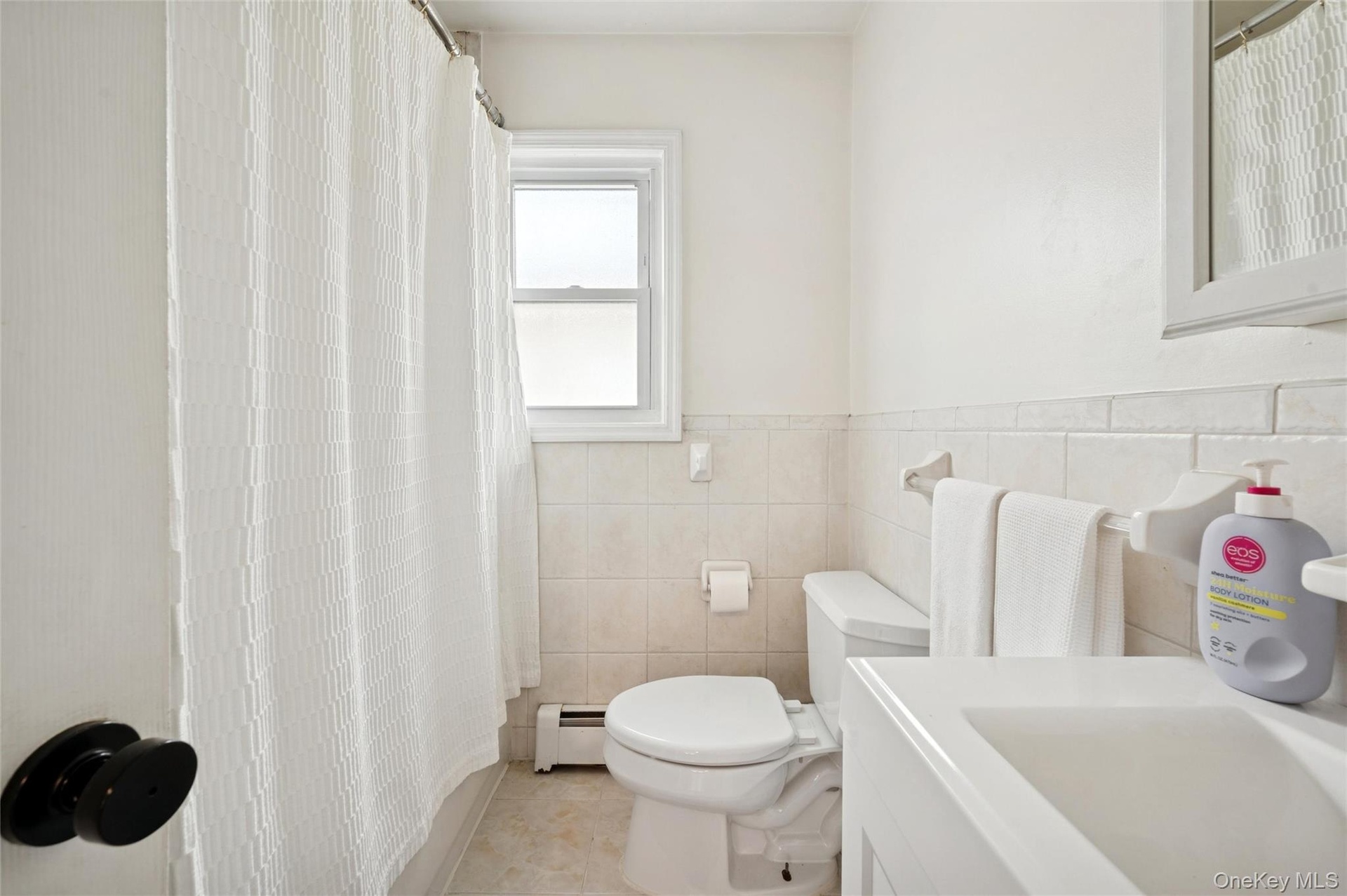 Full bath featuring a shower with shower curtain, vanity, a baseboard radiator, light tile patterned floors, and tile walls