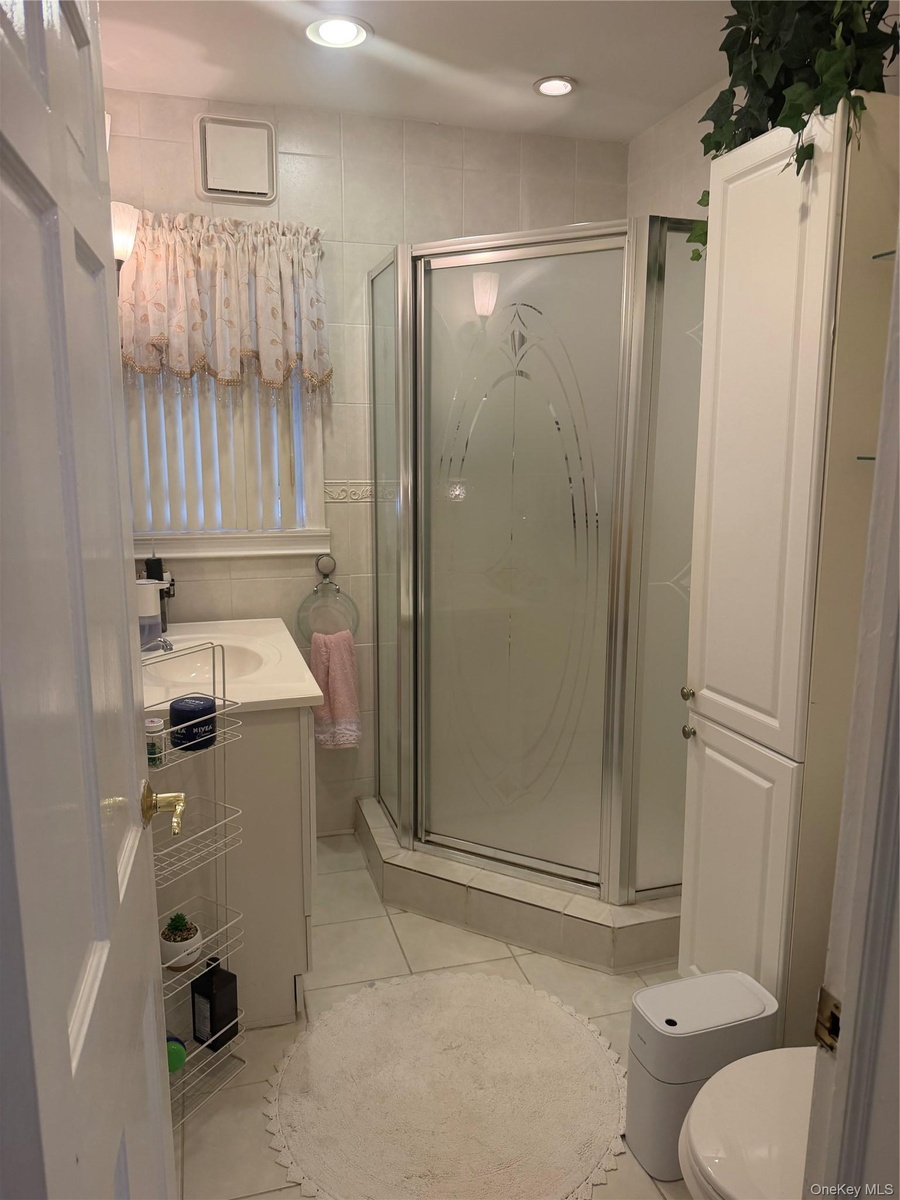 Tiled bathroom featuring a corner shower with frosted glass doors, white vanity with integrated sink, and recessed lighting