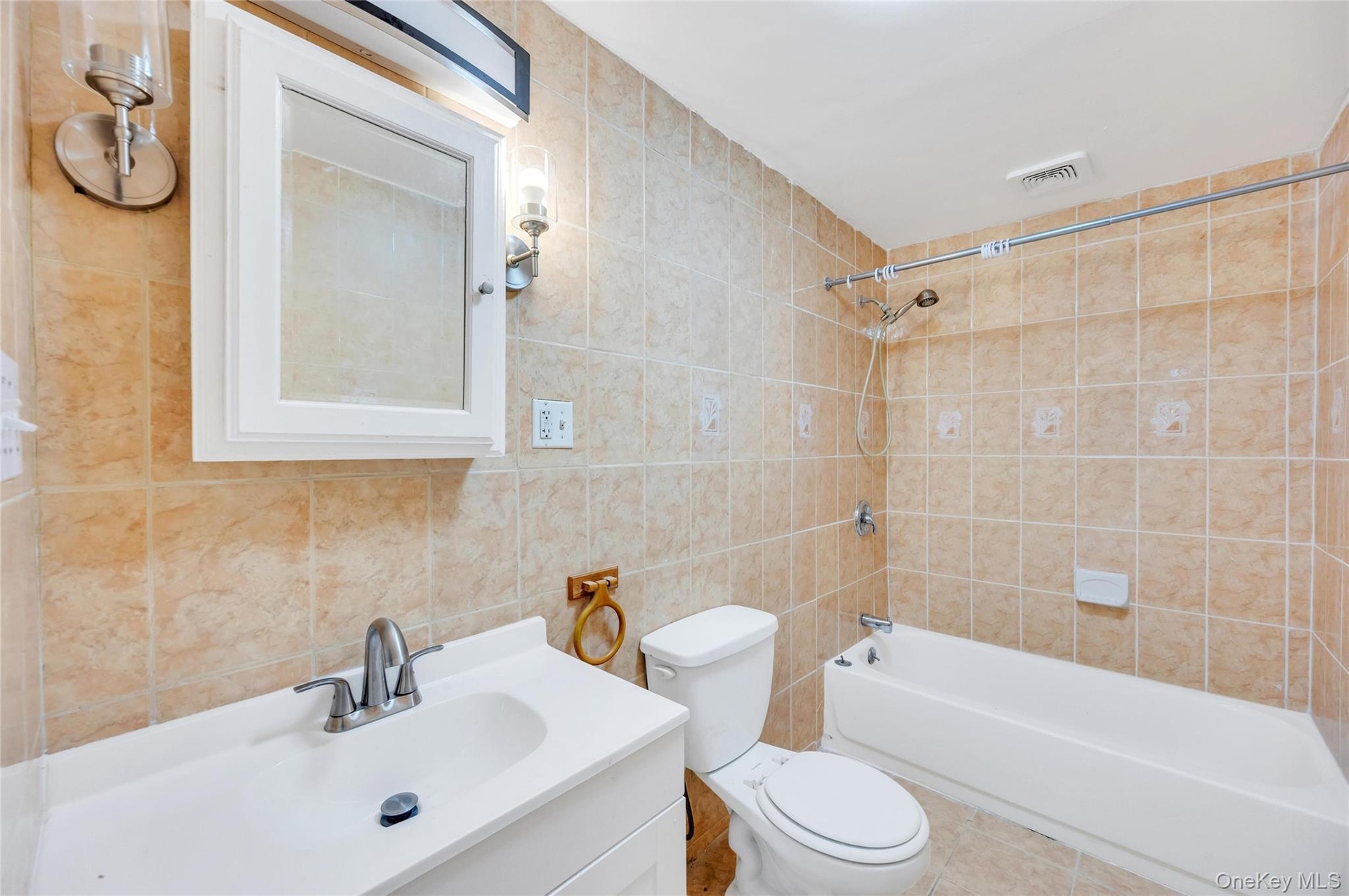 Bathroom featuring full-height beige tiled walls, white vanity with integrated sink, brushed nickel faucet, wall-mounted medicine cabinet, and a white