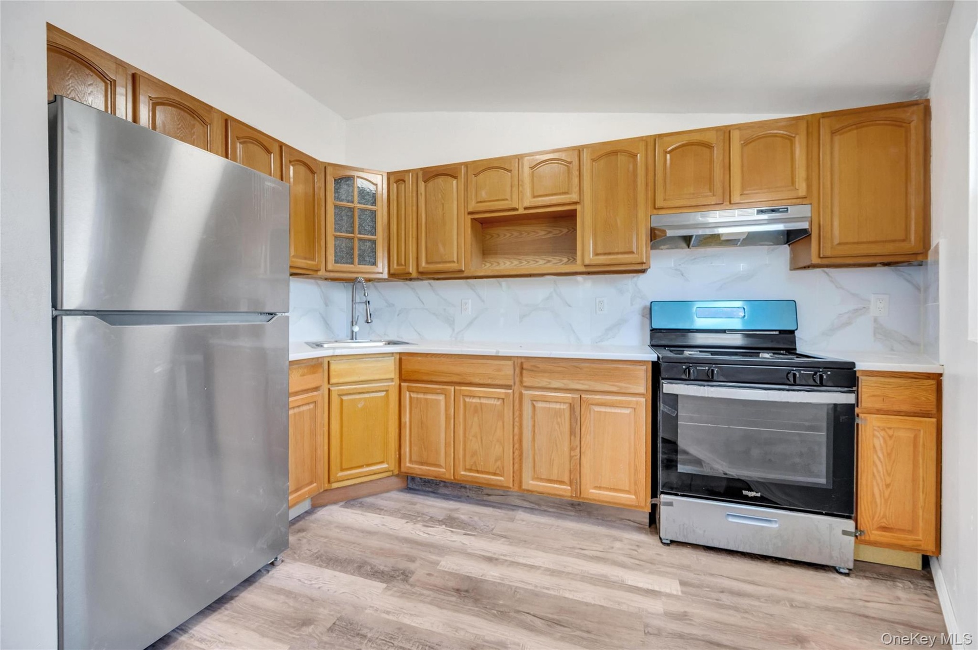 Kitchen featuring wood-finish cabinetry, stainless steel appliances, white countertops, and a full tile backsplash