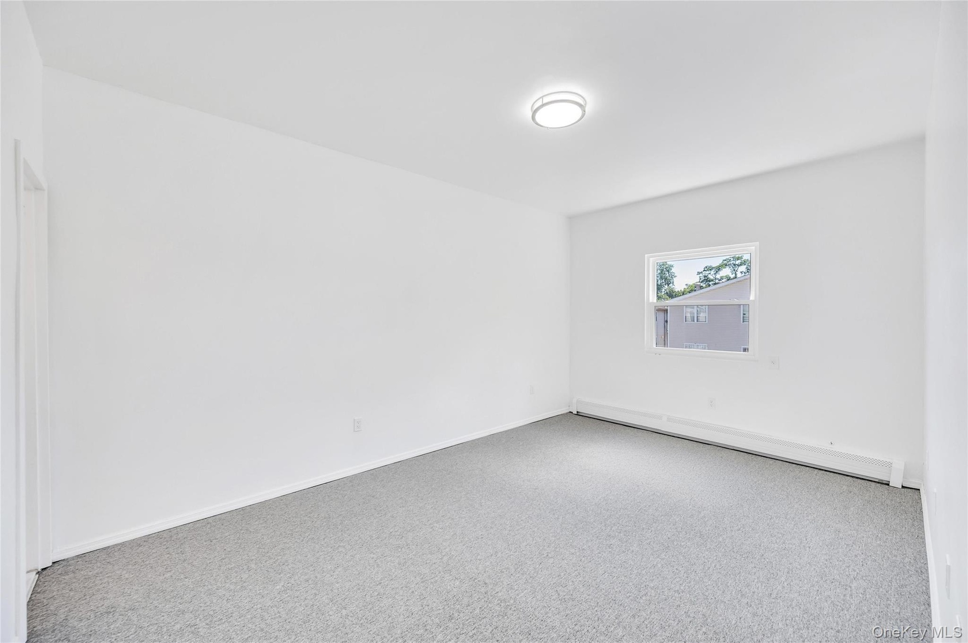 Bright room featuring a single window, white walls, gray carpet, a flush-mount ceiling light, and baseboard heating