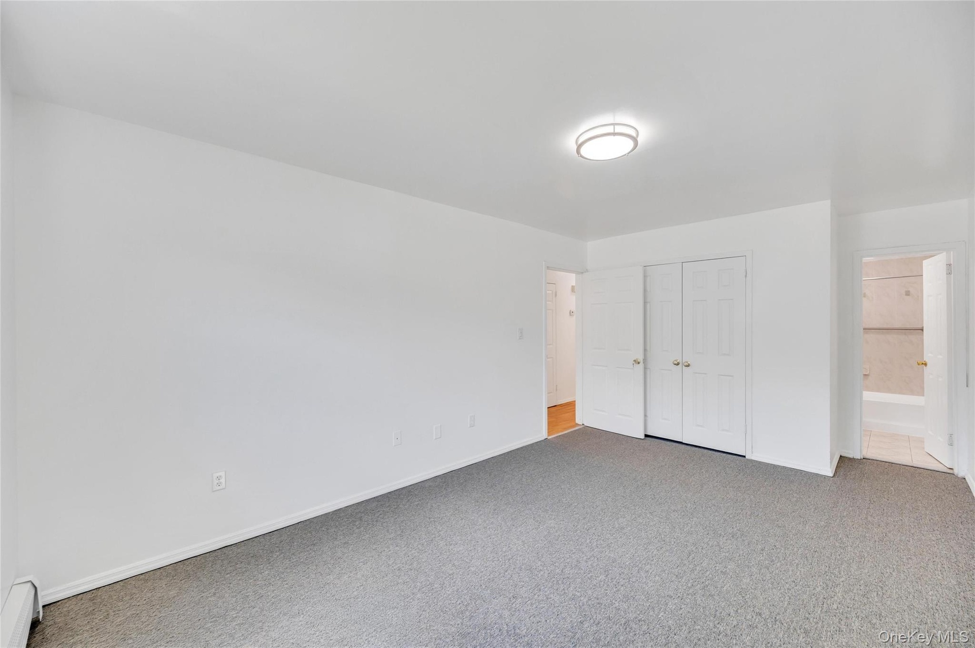 Spacious room featuring neutral carpeting, white walls, and a modern ceiling light fixture