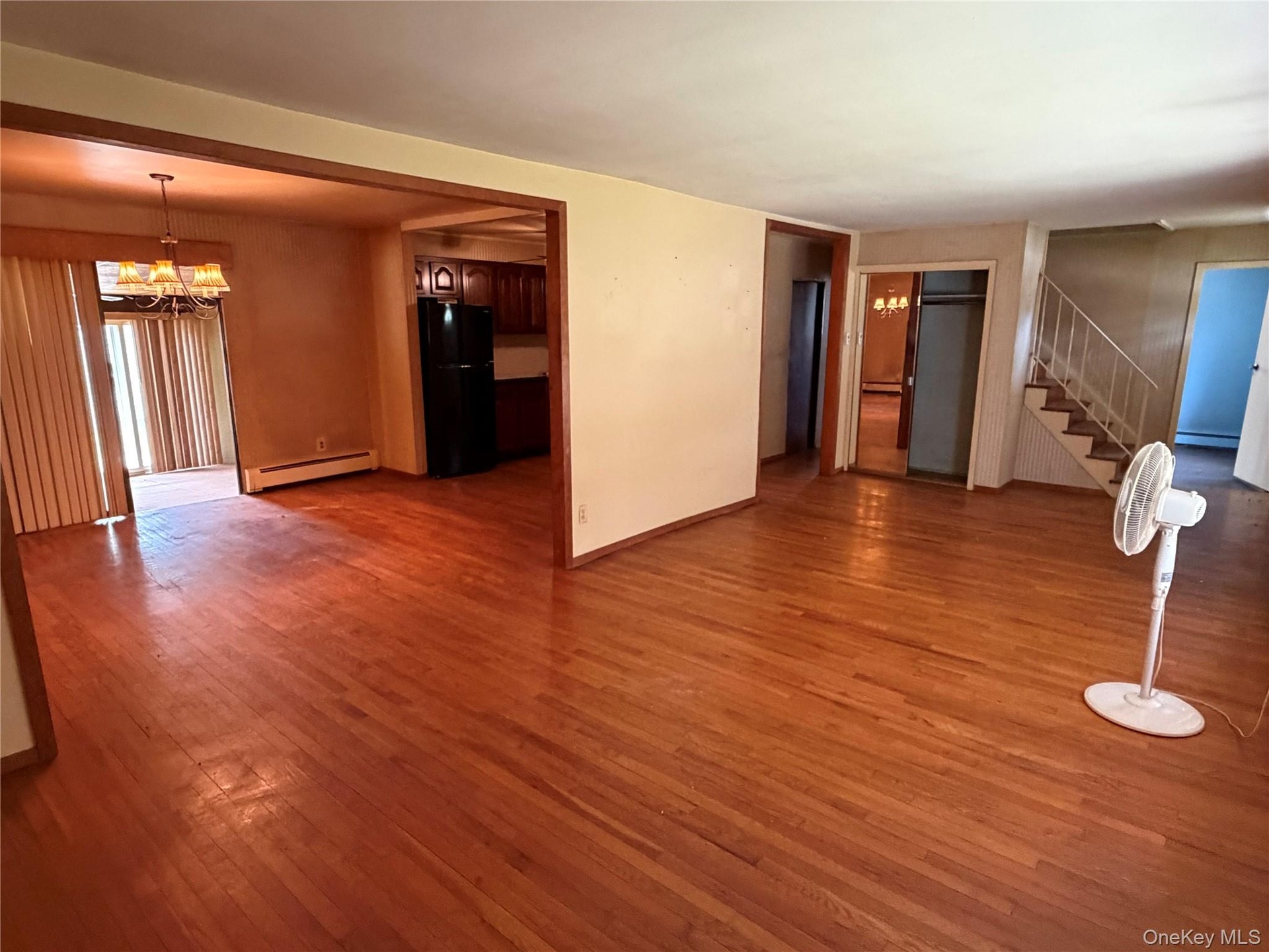 Expansive main living area featuring wood-finish flooring, a staircase with metal railings, and a doorway leading to a kitchen with dark cabinetry and