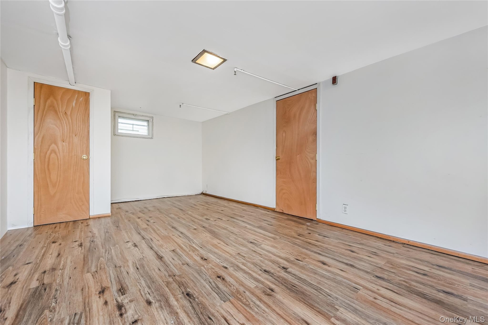 Spacious room featuring wood-finish flooring, white walls, and a recessed ceiling light