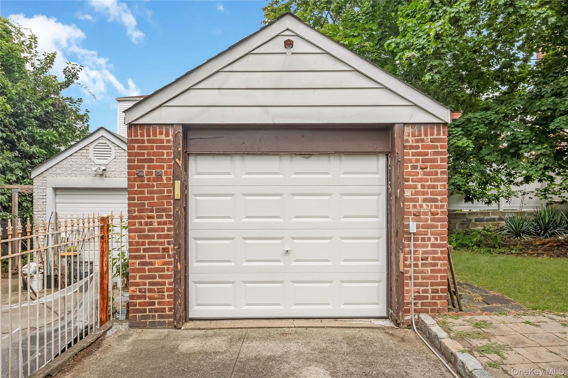 Brick garage featuring a white panel garage door and white siding gable