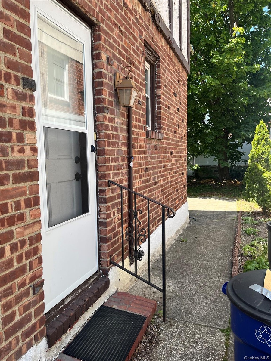Brick exterior featuring a white storm door, decorative wrought iron handrail, and an exterior wall lantern