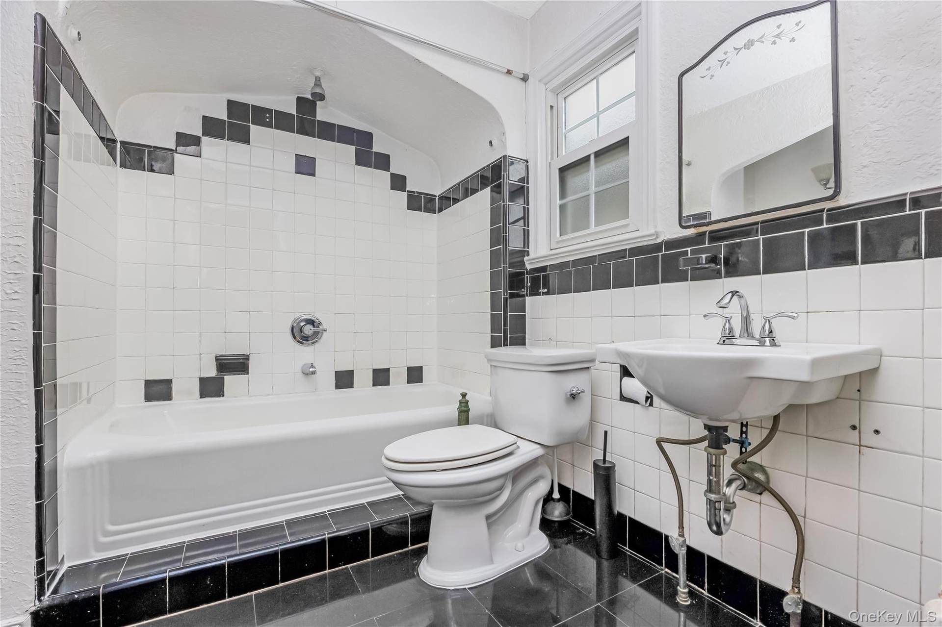 Bathroom with full bathtub, wall-mounted sink, and a black and white tile design