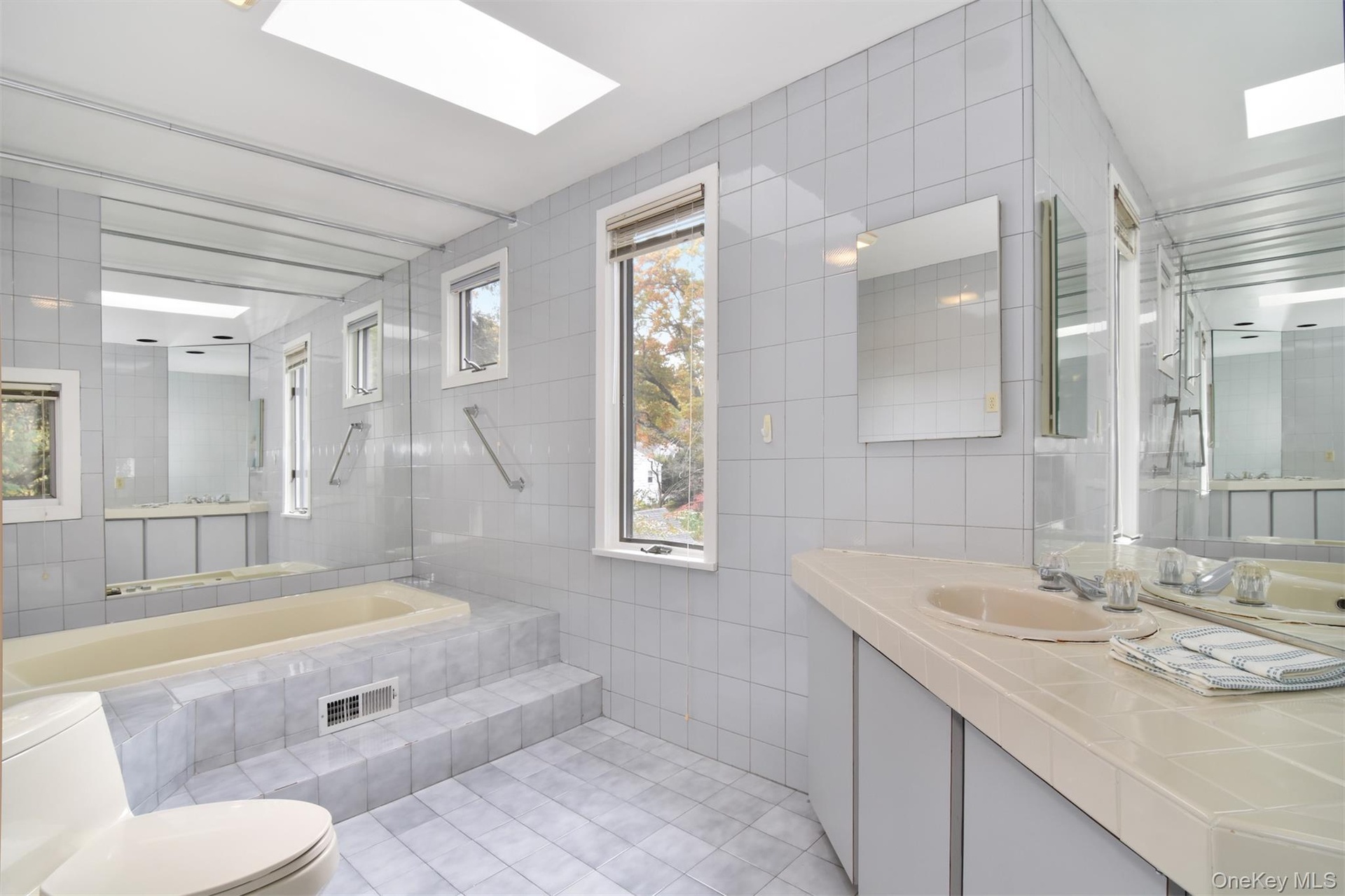 Primary Bathroom featuring tile walls, a skylight, light tile patterned floors, and vanity
