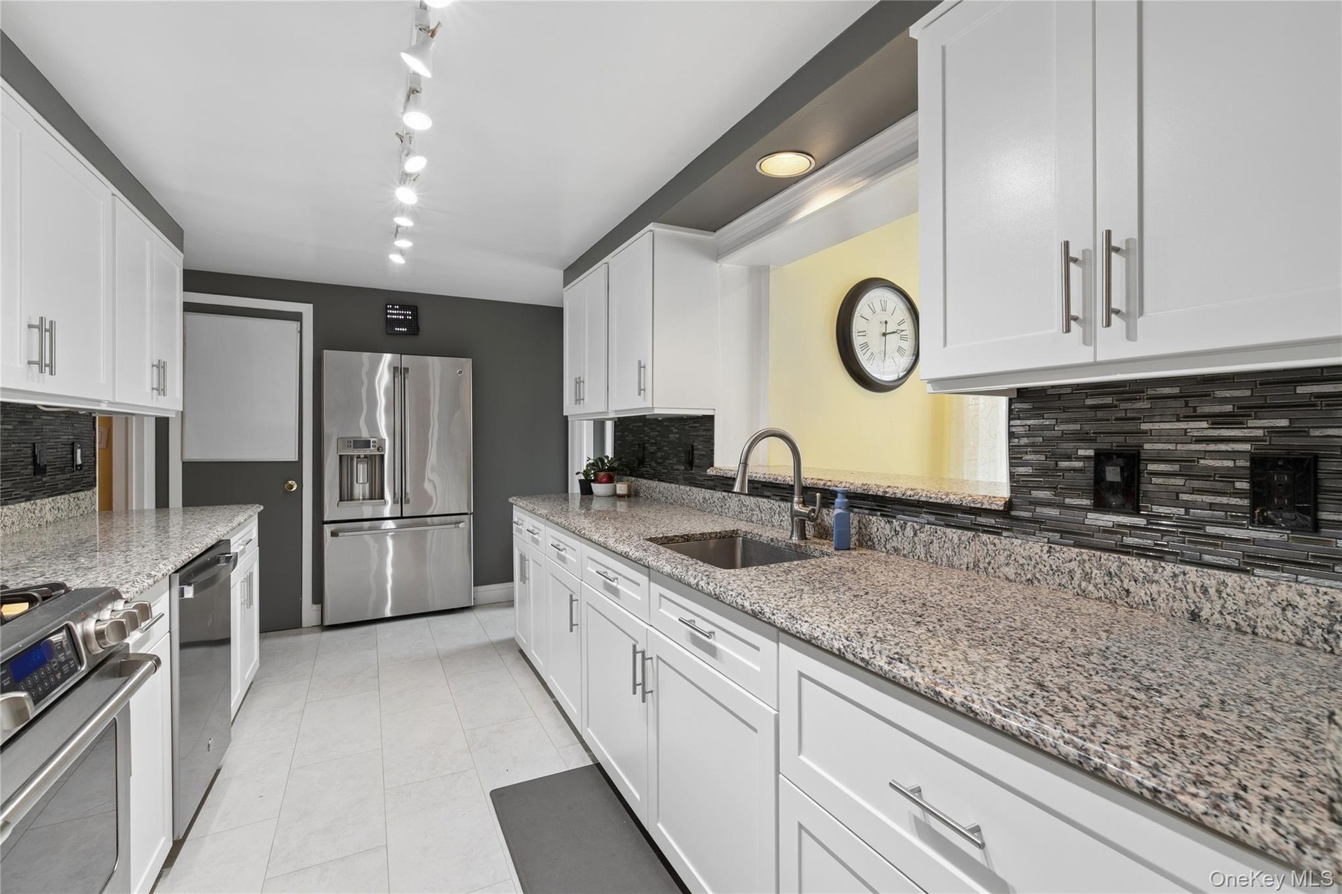 Galley kitchen with expansive white cabinetry, granite counters and updated appliances