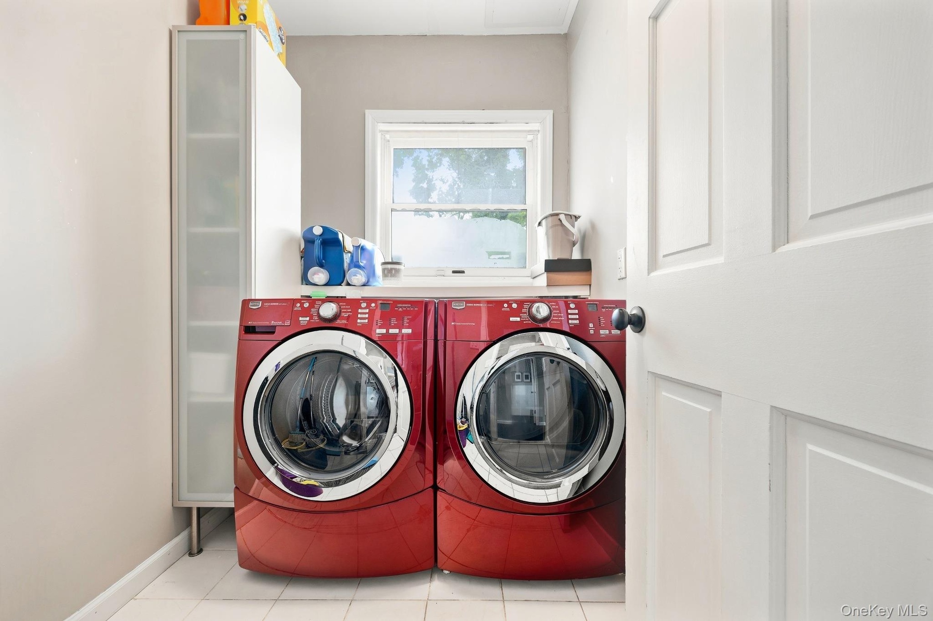 Laundry Room – Spacious laundry room featuring side-by-side front-loading washer and dryer, additional storage, and a window that fills the space with