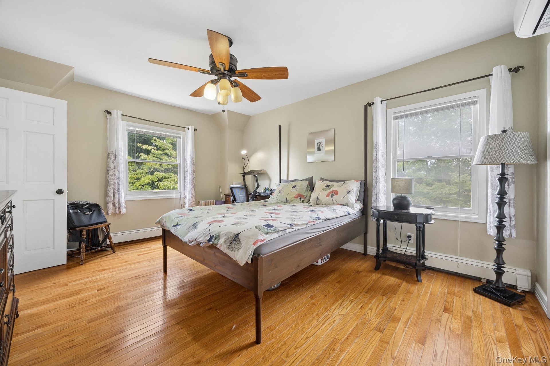 Spacious primary bedroom featuring rich hardwood flooring, multiple oversized windows that fill the room with natural light, and a generous layout off