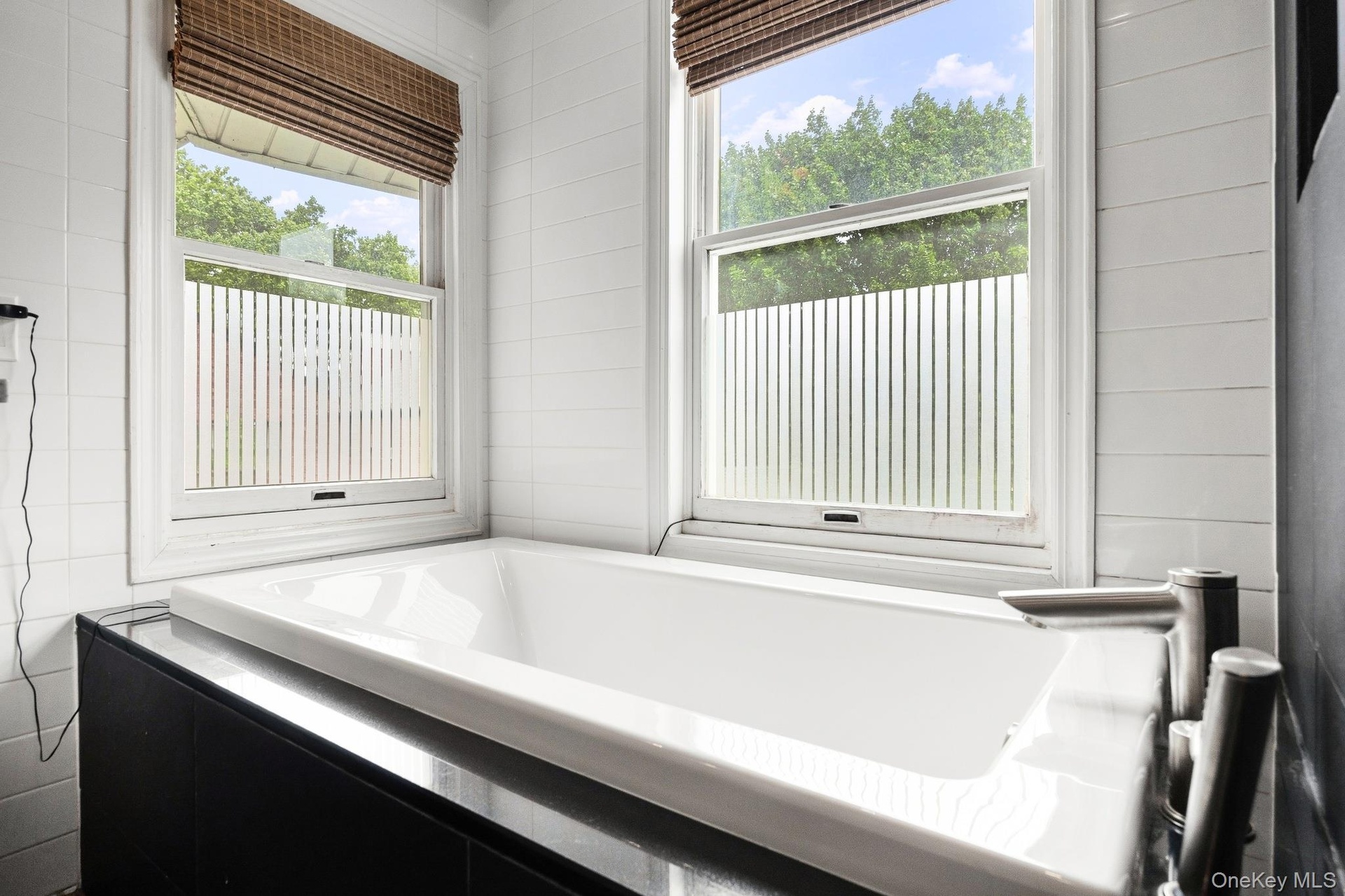 Spa-inspired primary bathroom featuring a soaking tub, oversized glass-enclosed walk-in shower, contemporary tile finishes, and abundant natural light