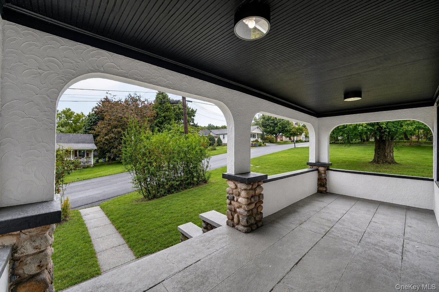 Inviting covered porch with a textured stucco finish and stone-clad pillars