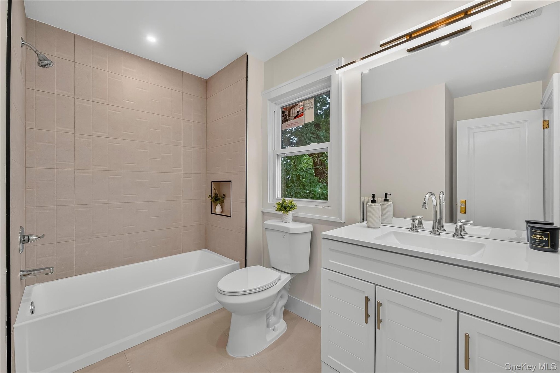 Bathroom featuring a white vanity with a quartz countertop, a large mirror with integrated lighting, a tub/shower combination with tiled walls, and a 