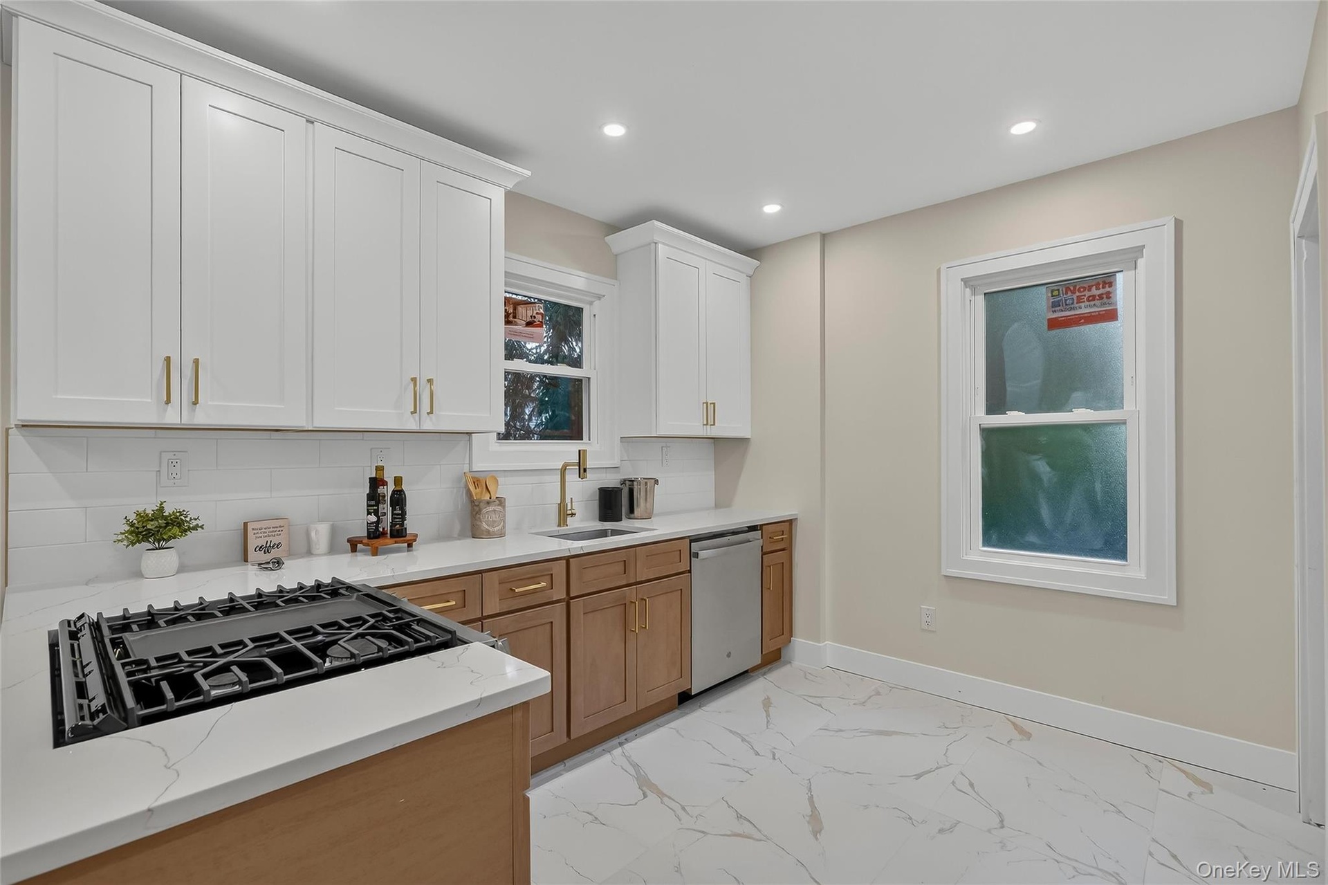 Modern kitchen featuring a gas cooktop, white upper cabinetry, natural wood-finish lower cabinetry, and light-toned countertops