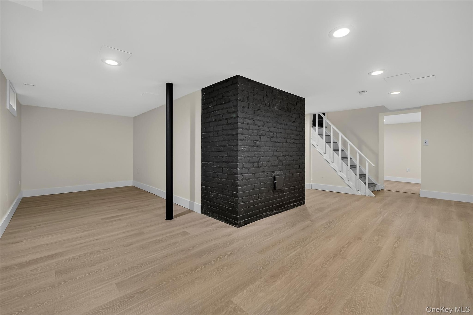 Expansive finished basement featuring wood-finish flooring, recessed lighting, and a prominent black brick accent wall