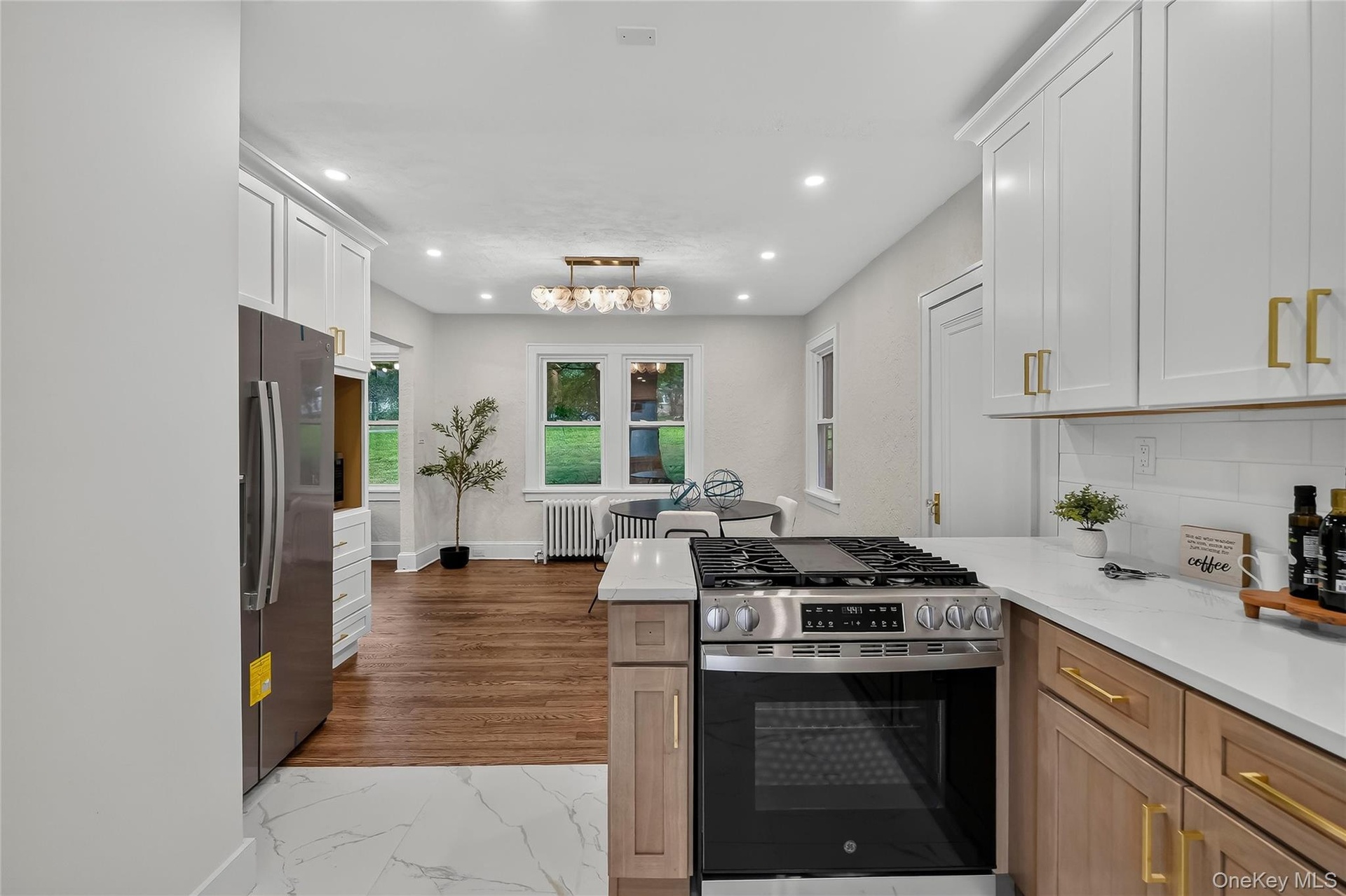 Modern kitchen featuring white shaker upper cabinetry and natural wood lower cabinetry with gold-tone hardware