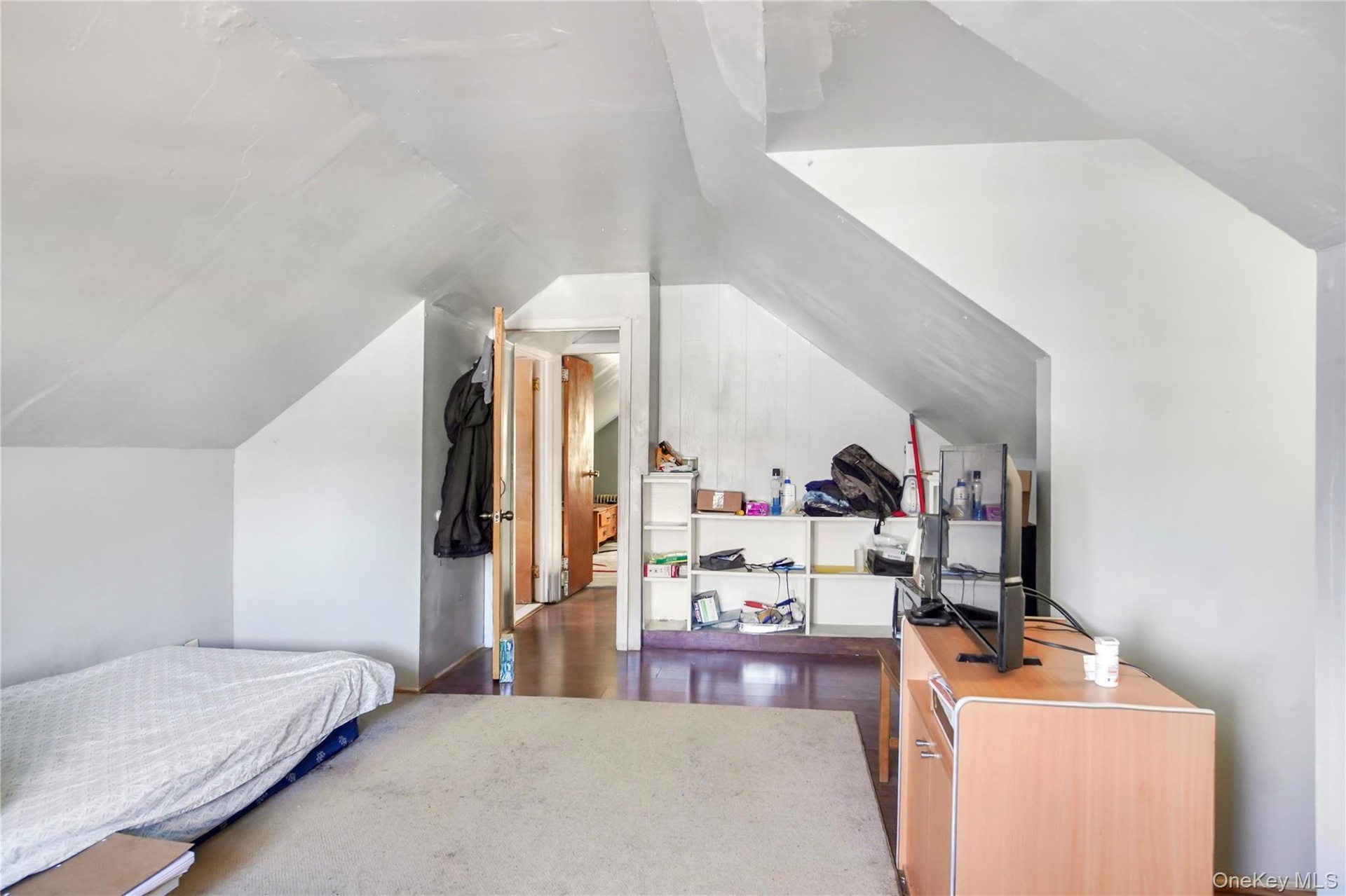 Spacious room featuring sloped ceilings, light-toned wall finishes, wood-finish flooring, and a doorway leading to an additional area