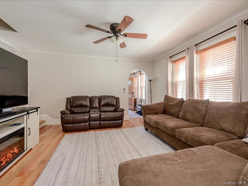 Living area featuring wood-finish flooring, a ceiling fan with light fixture, and archway entry