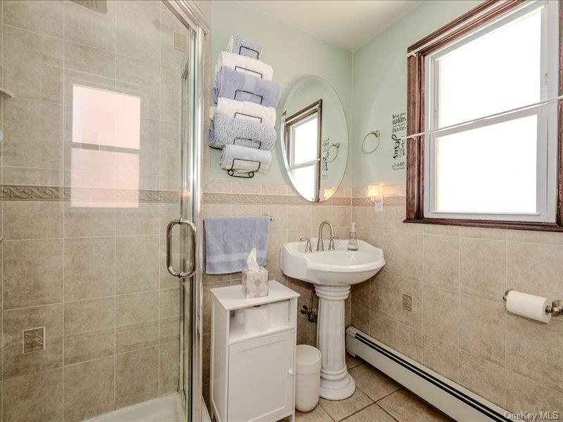 1st Floor Bathroom featuring a glass-enclosed shower, pedestal sink with a chrome faucet, and tiled walls with decorative banding