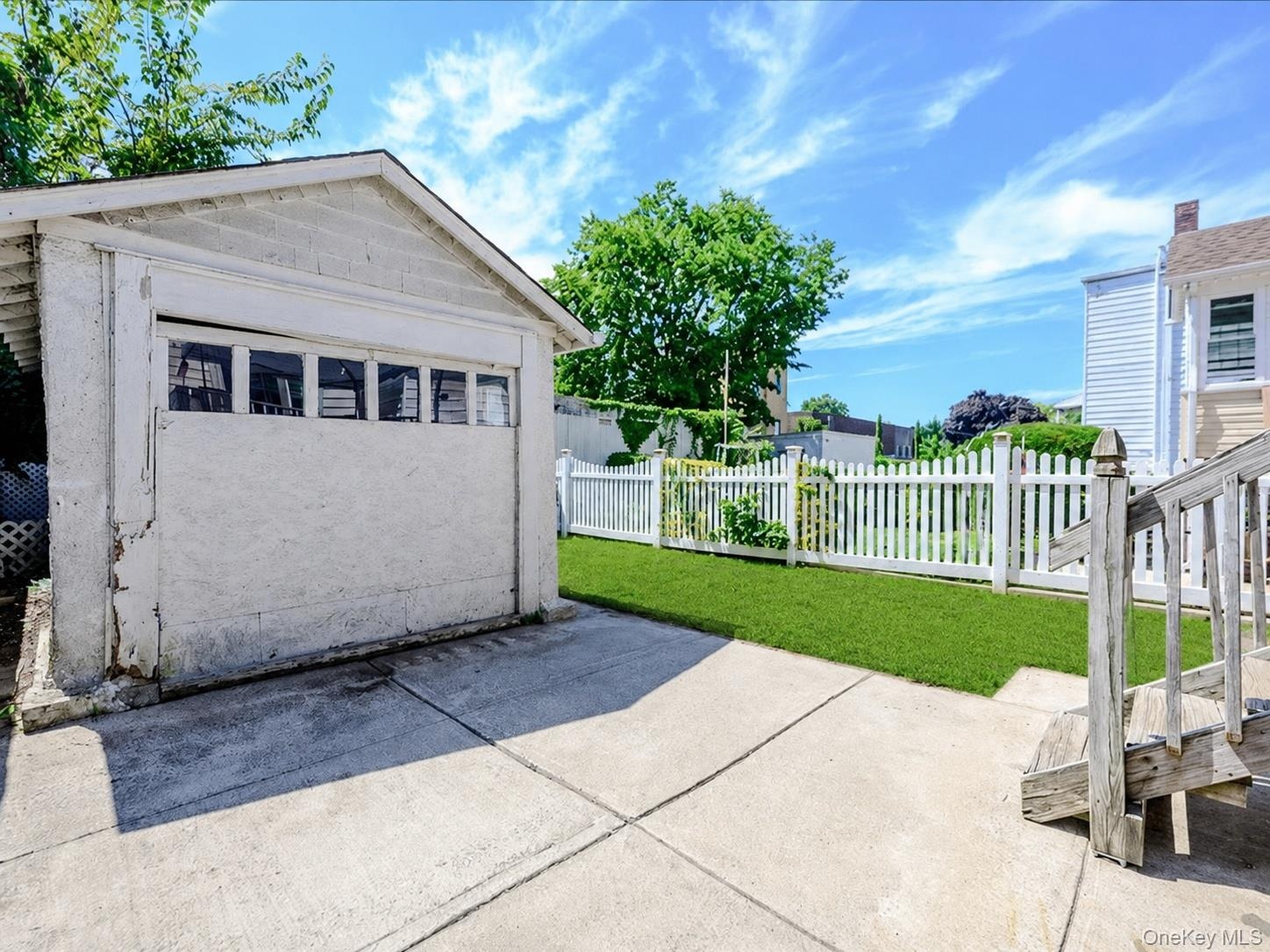 Detached garage with upper window panels, concrete driveway, and a fenced grassy yard. ai generated