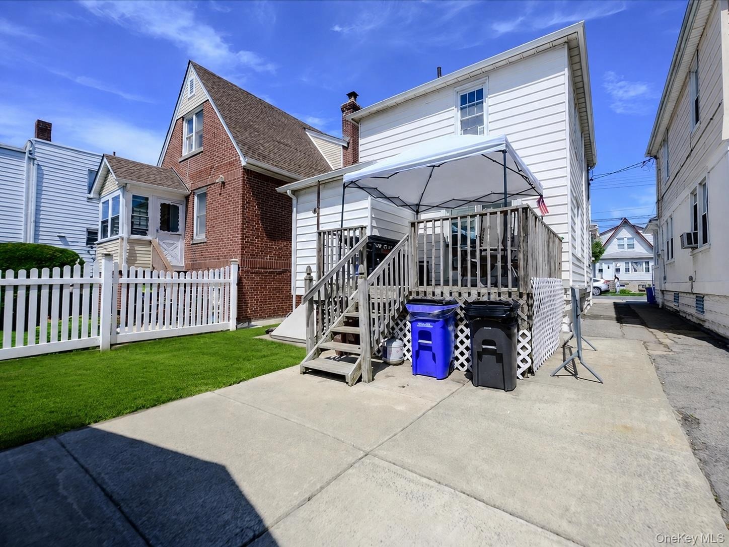 Rear yard featuring a wood deck with stairs, white picket fence, and a grass lawn. ai generated.