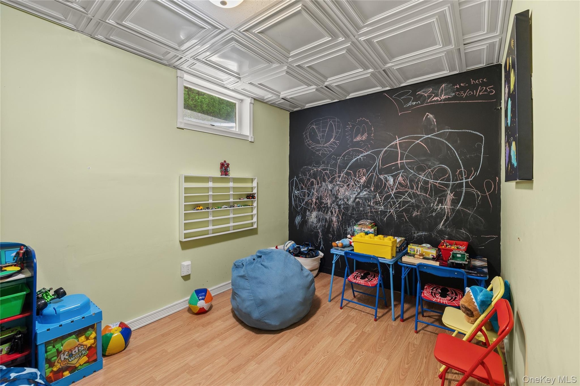 Room featuring wood-finish flooring, a decorative ceiling with square panels, and a chalkboard wall
