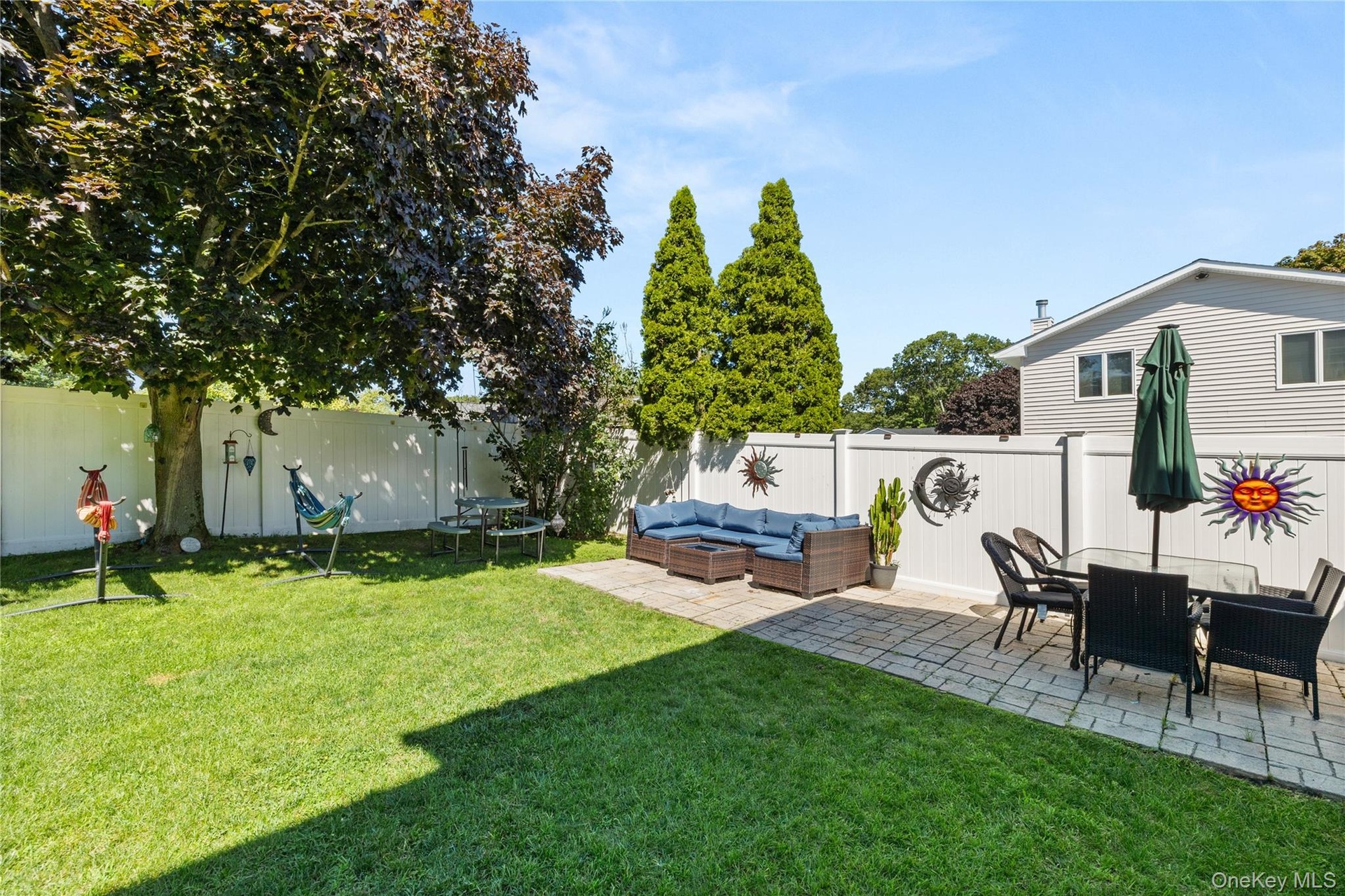 Expansive backyard featuring a manicured lawn, a large shade tree, and a white privacy fence