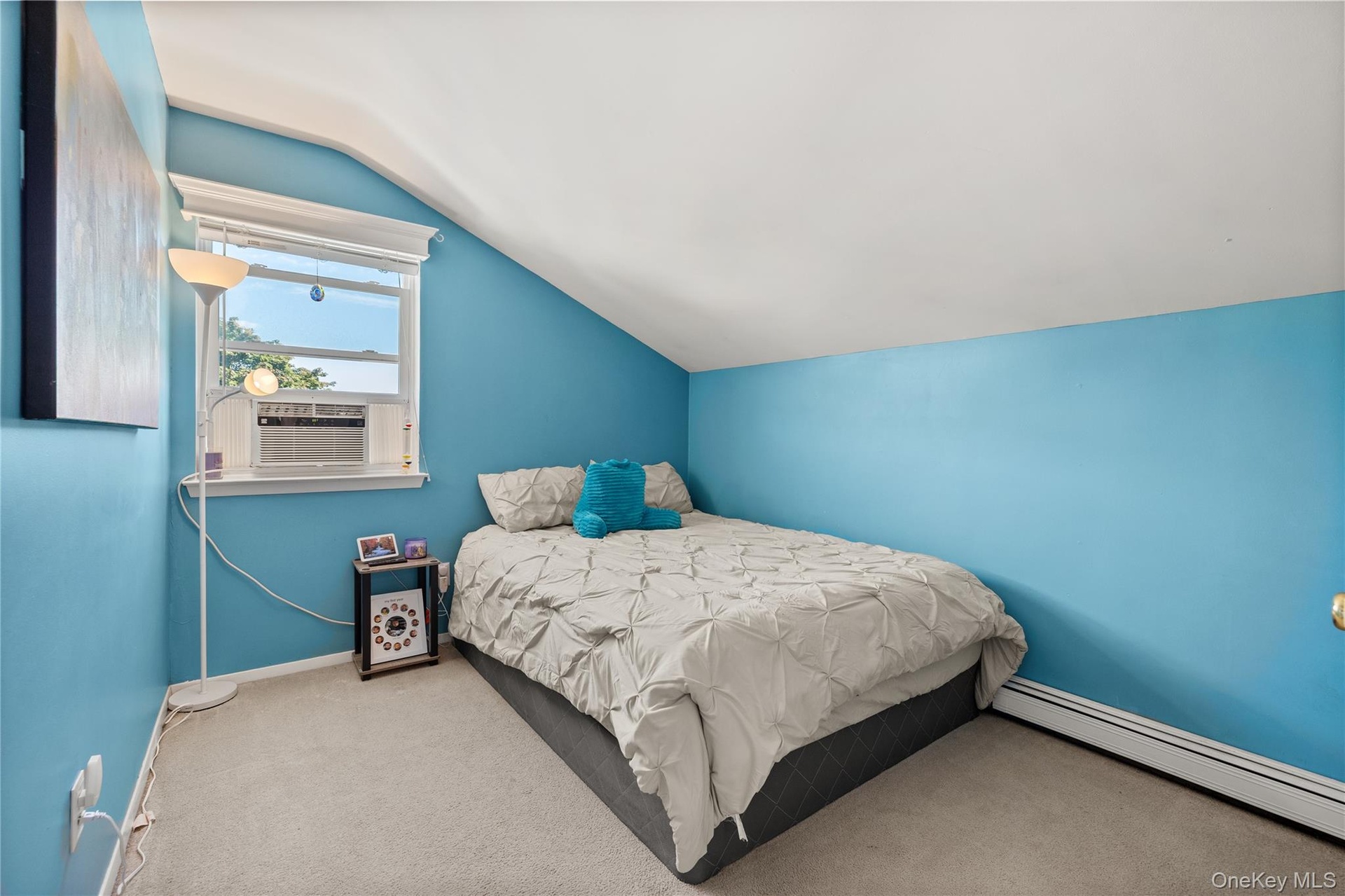 Carpeted room featuring a window with an air conditioning unit, sloped ceiling, and baseboard heating
