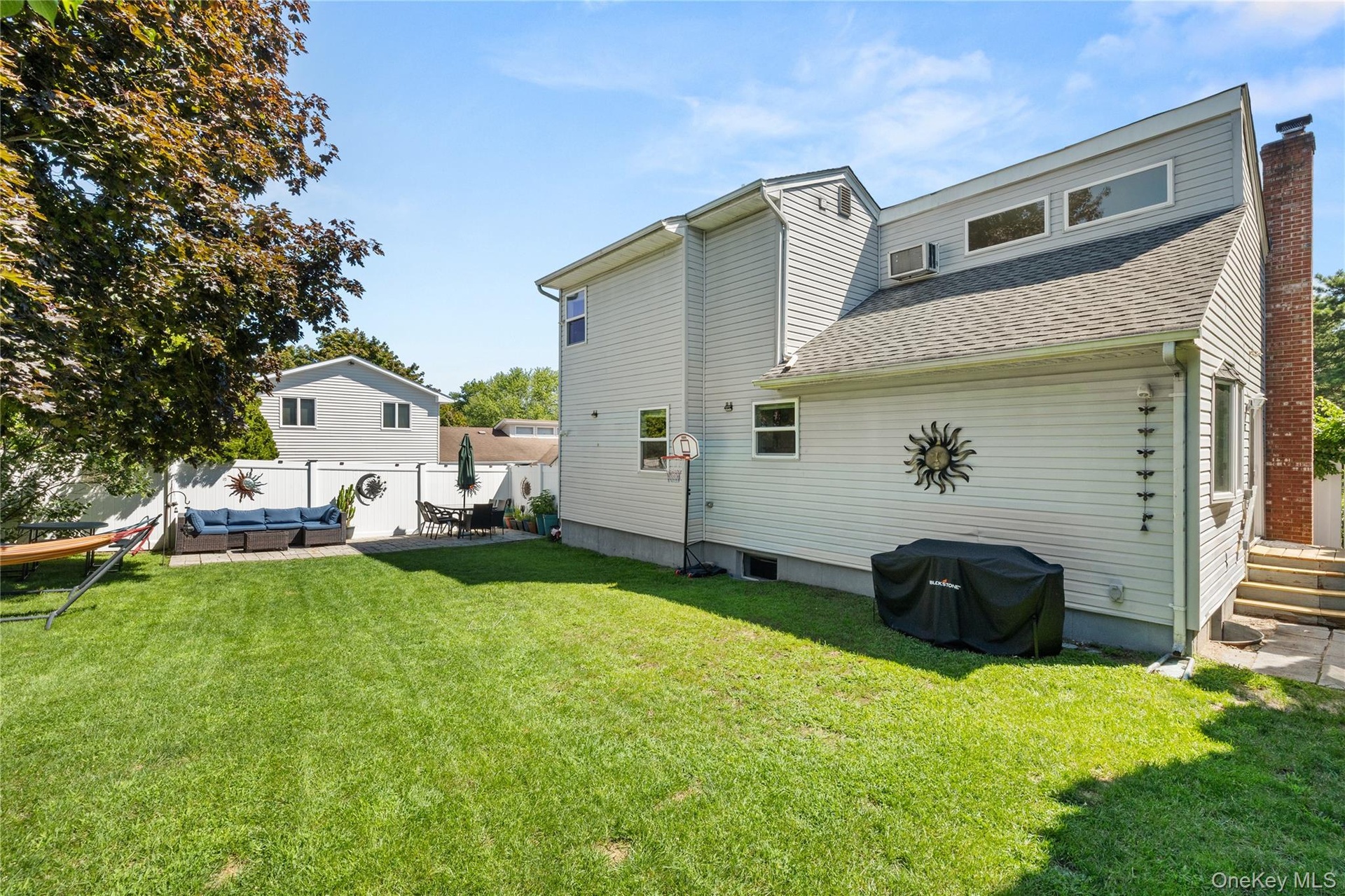 Expansive backyard featuring a manicured lawn, white privacy fencing, and a dedicated patio area