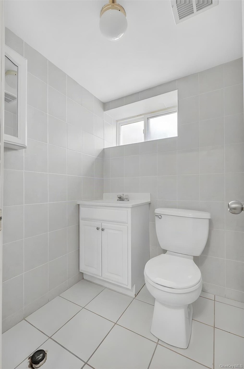 Bright and functional bathroom featuring white subway tile walls, ceramic tile flooring, a white vanity cabinet with dual doors and hardware, and a st