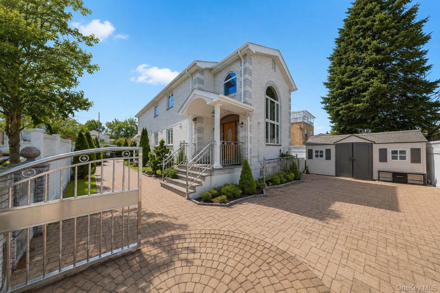 French Colonial residence showcasing a brick paver driveway and circular turret with arched windows