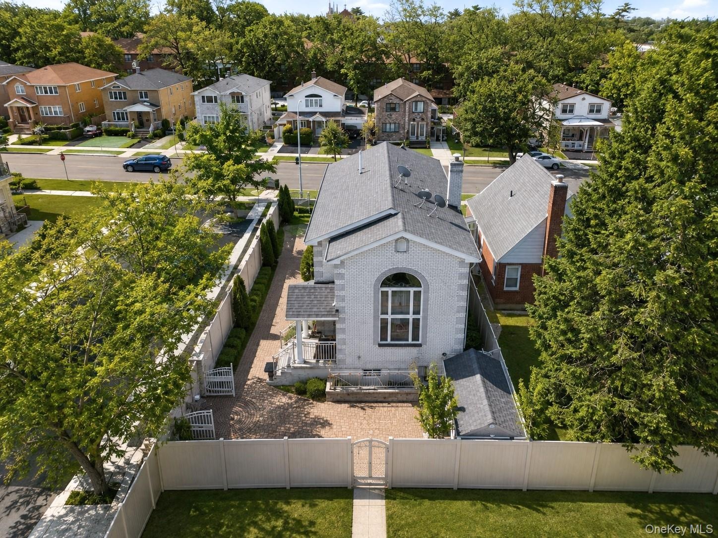 Brick Colonial residence showcasing a gabled roofline, arched entryway with transom windows, and a professionally landscaped front courtyard framed by