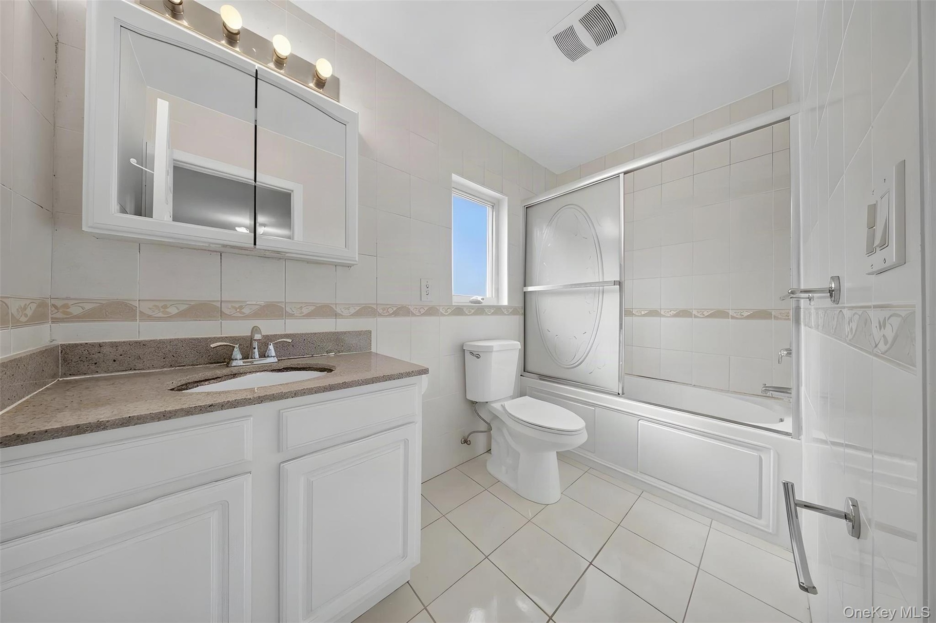 Spa-inspired primary bathroom featuring a white vanity with granite countertop, medicine cabinet with mirrored glass doors, ceramic tile flooring, and